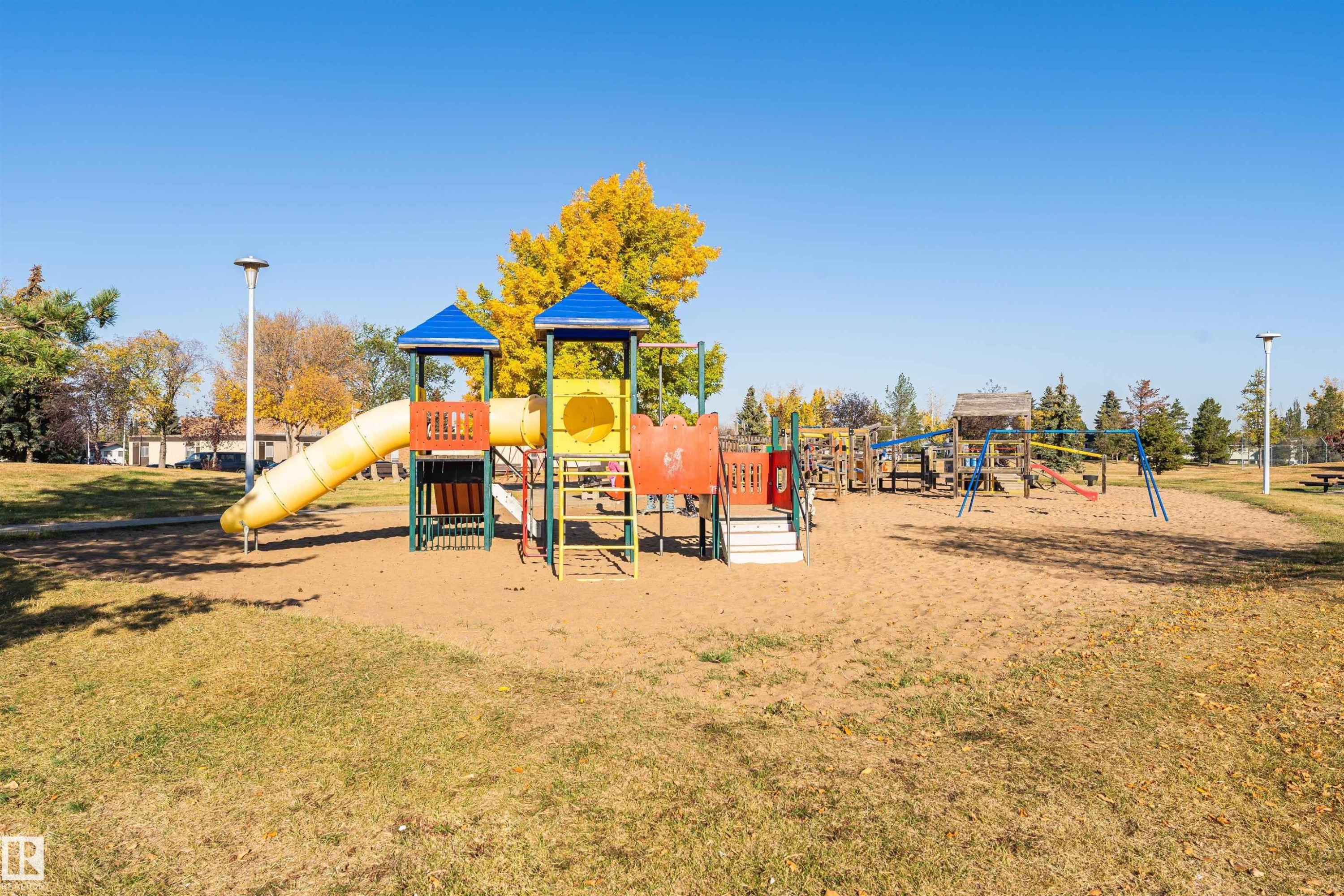 Community playground featuring multiple play structures, sand base, and surrounding green space with mature trees - 1612 80A Street, Edmonton, AB