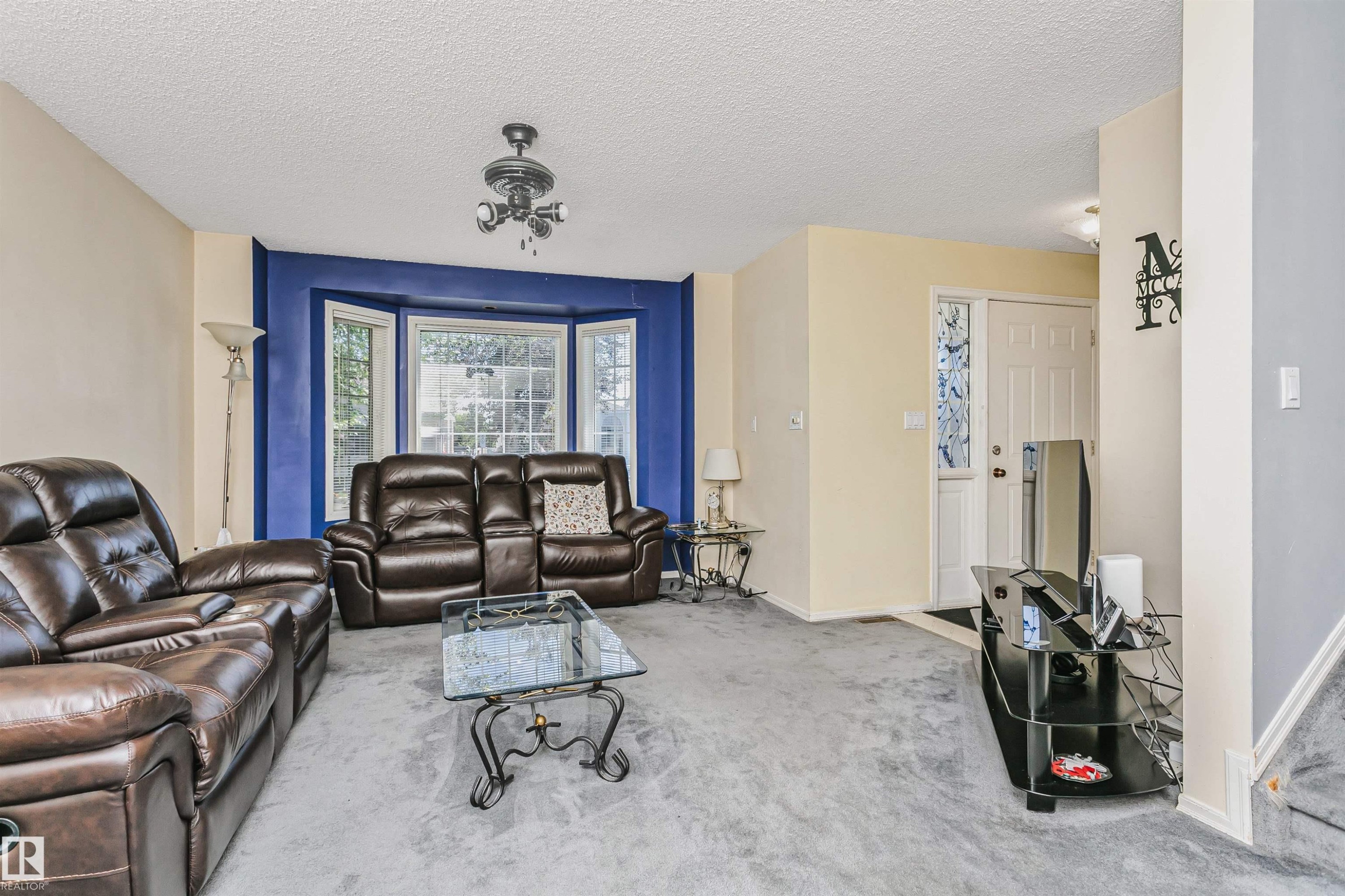 Living area featuring a prominent bay window, neutral wall tones with an accent wall, ceiling fan light fixture, and carpet flooring - 1612 80A Street, Edmonton, AB
