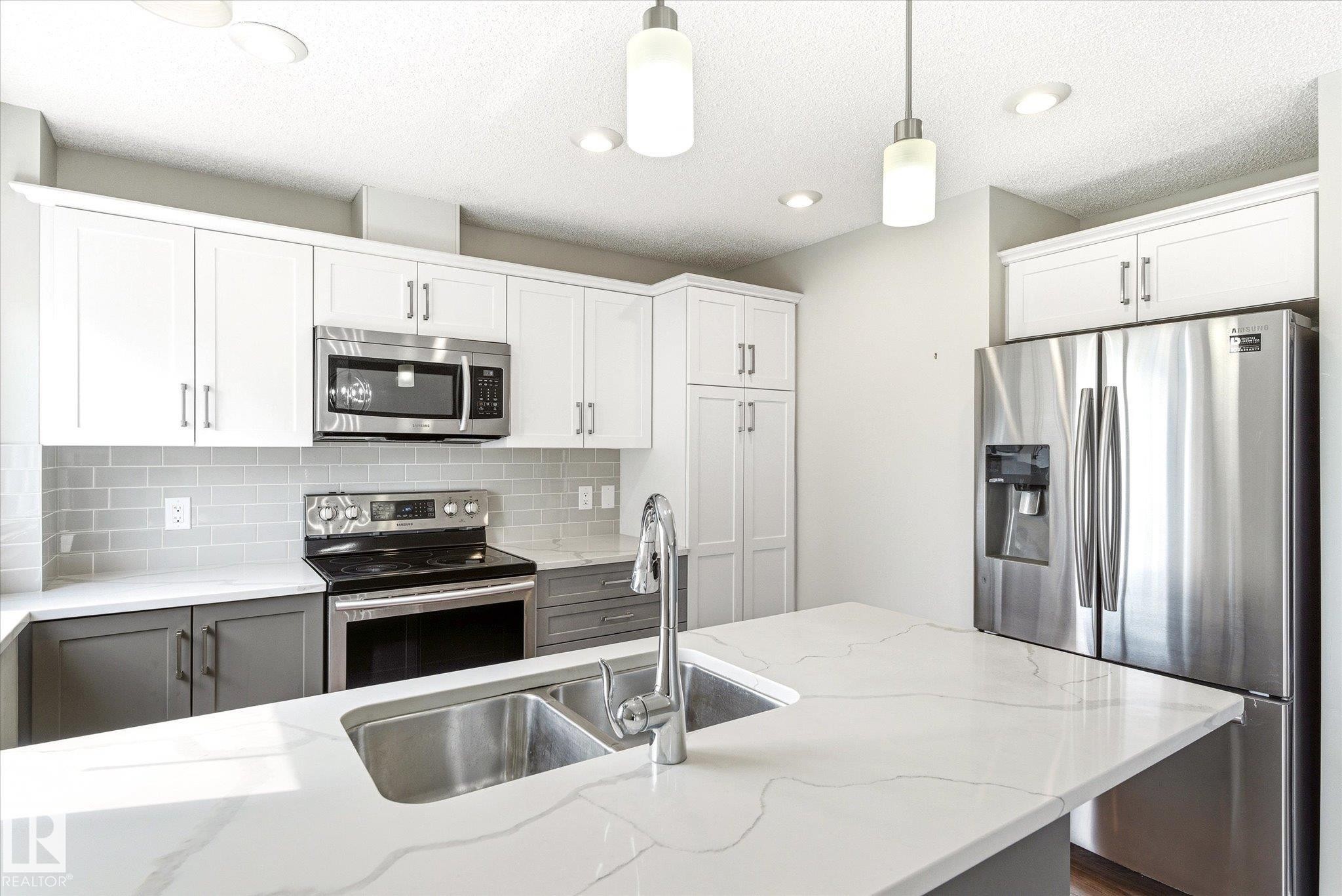 Modern kitchen featuring an island with a double basin stainless steel sink, white quartz countertops, and pendant lighting - 47 330 Bulyea Road, Edmonton, AB - Indoor Photo Showing Kitchen With Stainless Steel Kitchen With Double Sink With Upgraded Kitchen