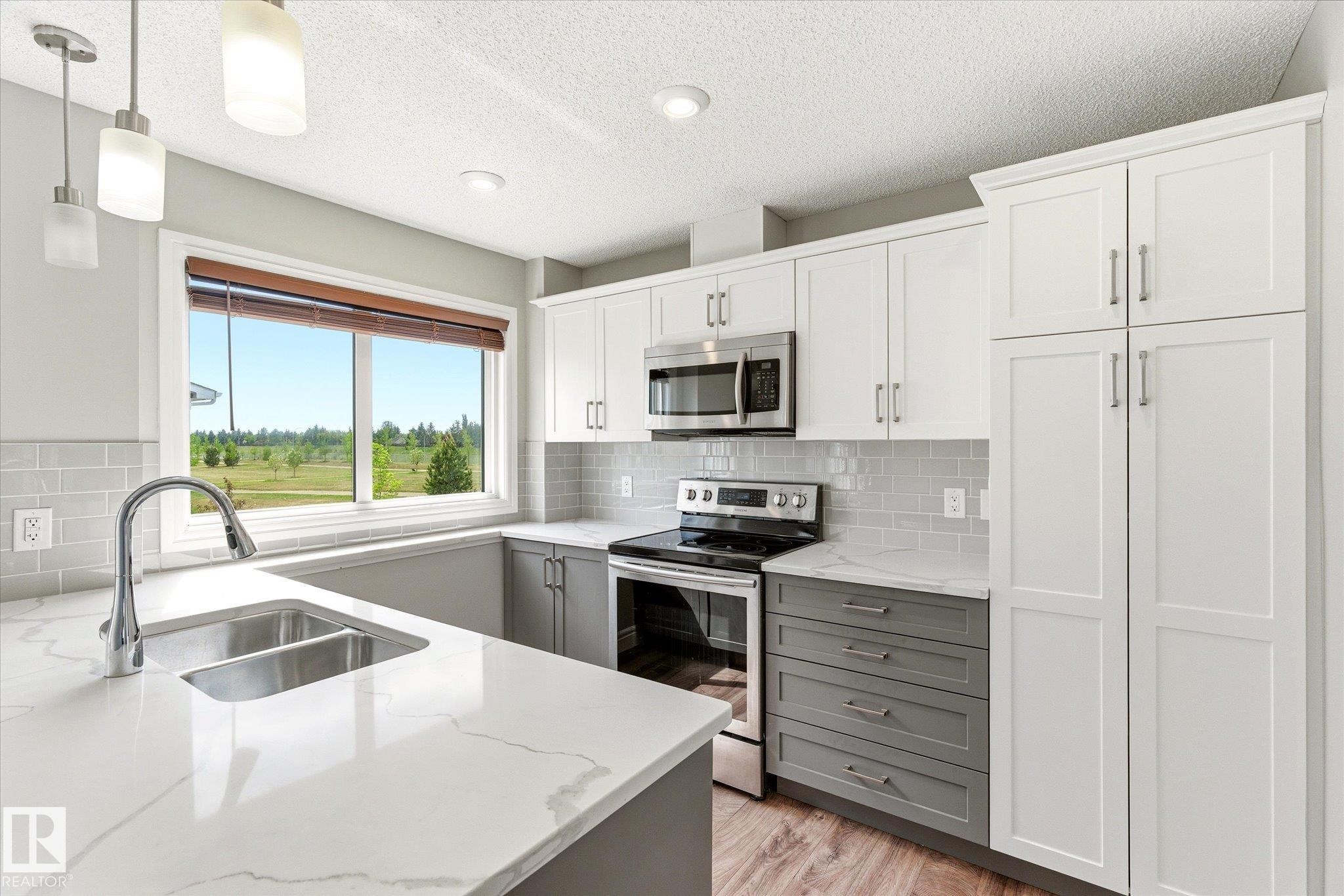 Modern kitchen featuring white and gray cabinetry, stainless steel appliances, a double basin sink, and wood-finish flooring - 47 330 Bulyea Road, Edmonton, AB - Indoor Photo Showing Kitchen With Double Sink With Upgraded Kitchen
