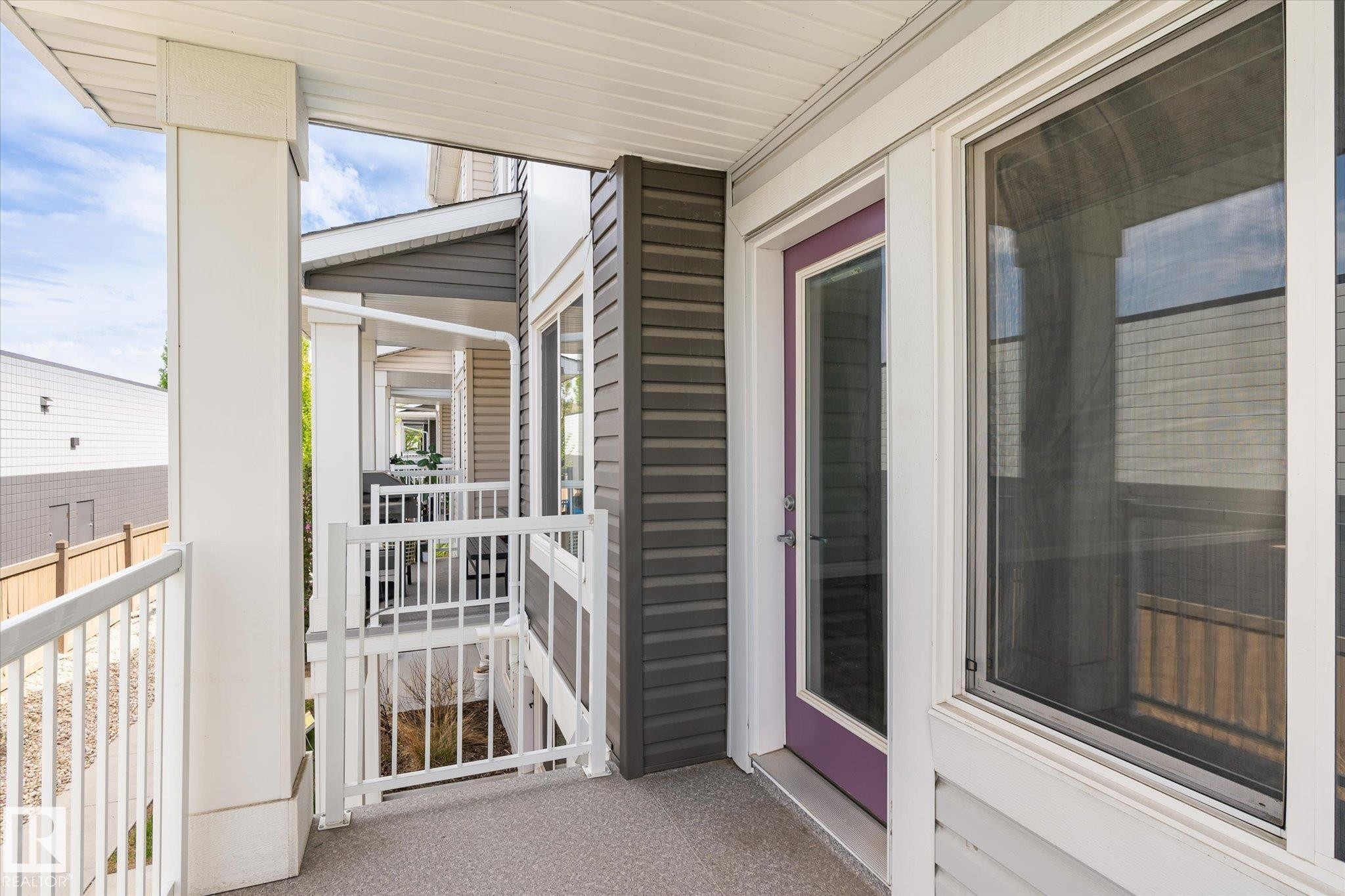 Exterior balcony featuring a textured concrete surface, white aluminum railings, and a purple-framed glass door - 47 330 Bulyea Road, Edmonton, AB - Outdoor With Balcony With Exterior
