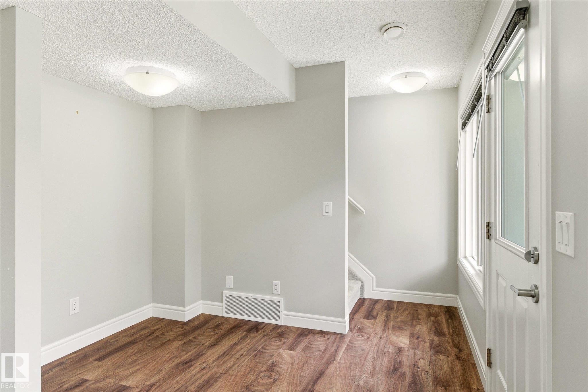 Entry area featuring wood-finish flooring, light gray walls, white baseboards, and a glass-paneled door with window blinds - 47 330 Bulyea Road, Edmonton, AB - Indoor Photo Showing Other Room