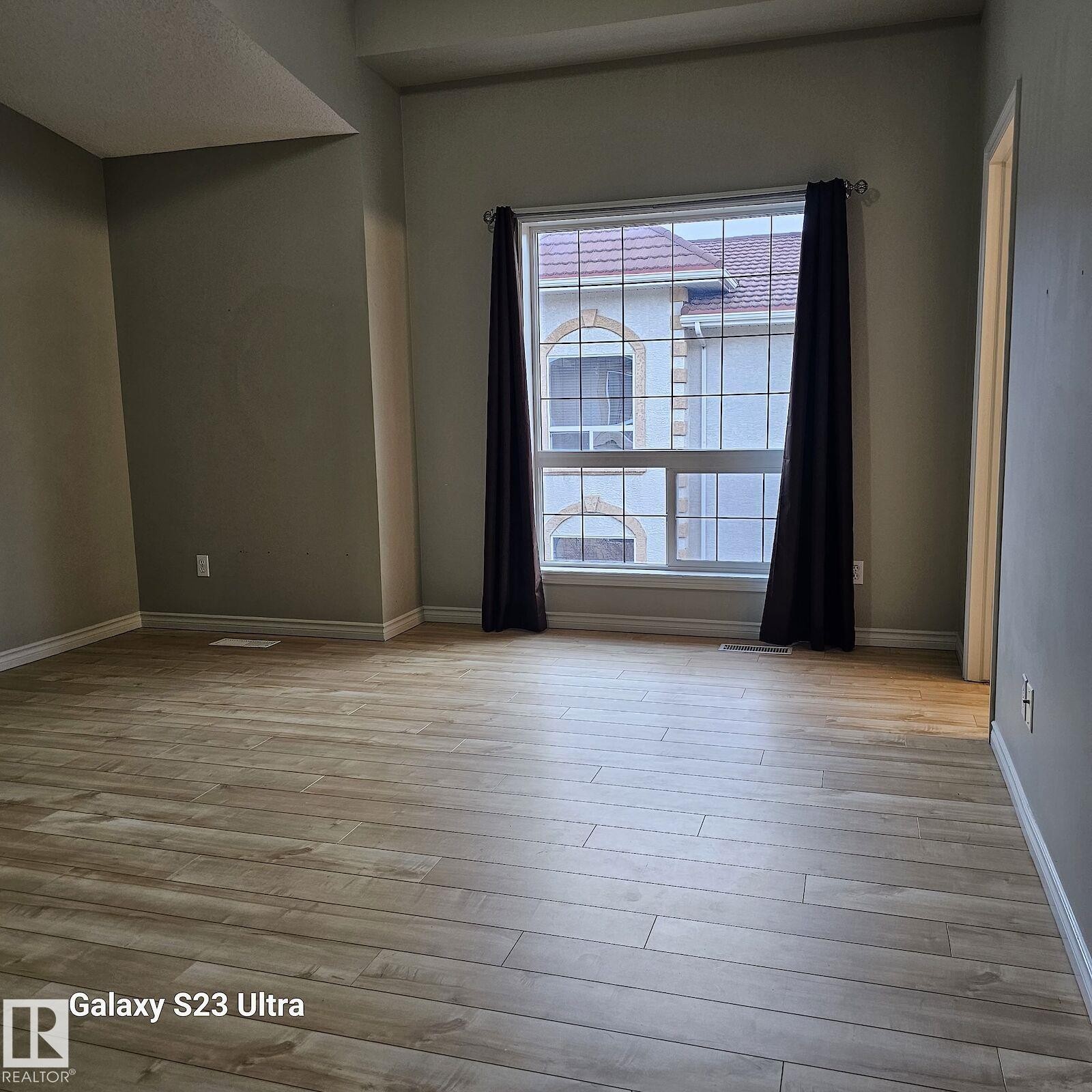 Spacious room featuring light wood-finish flooring, a large multi-pane window, and high ceilings - 99 13825 155 Avenue, Edmonton, AB