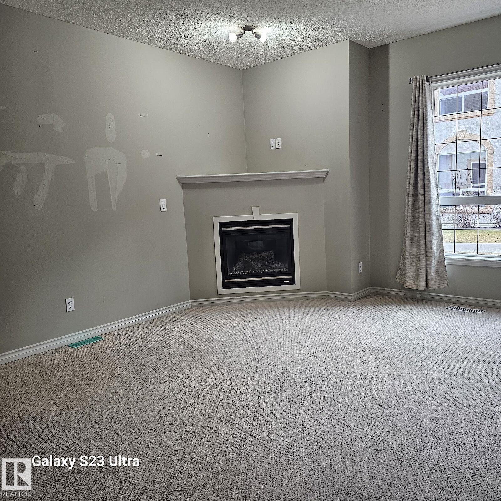 Living area featuring an integrated fireplace with a white mantel, light grey walls, and neutral carpeting - 99 13825 155 Avenue, Edmonton, AB