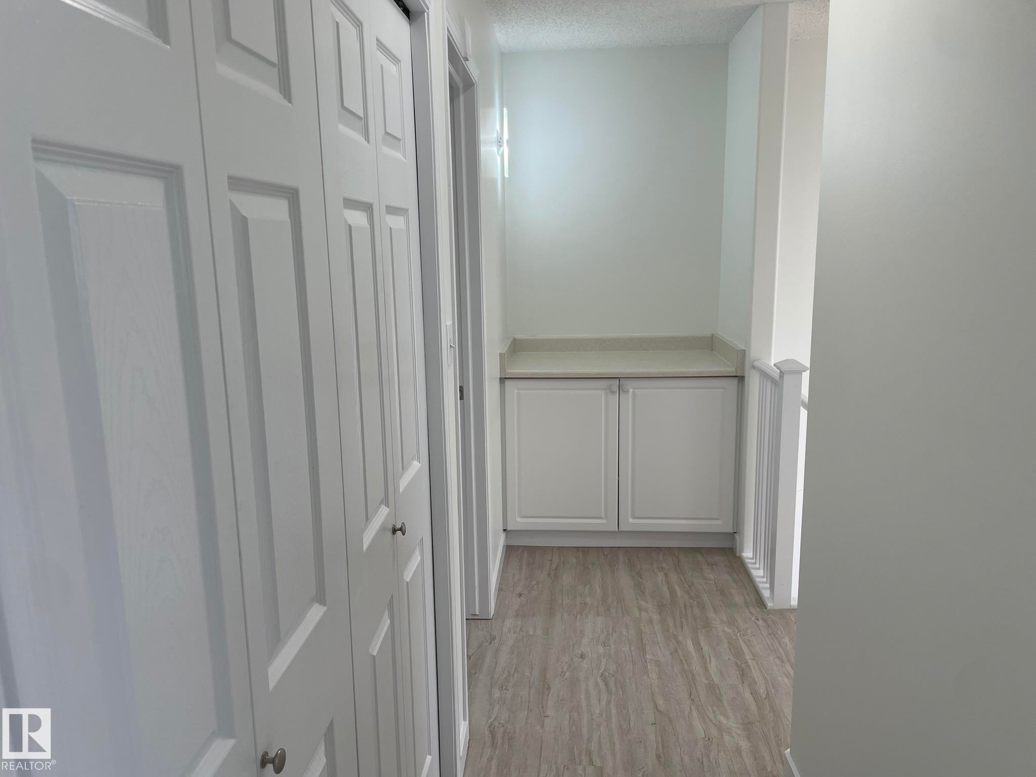 Hallway featuring white bi-fold doors, wood-finish flooring, and a built-in storage cabinet with a light-toned countertop - 2 1295 Carter Crest Road, Edmonton, AB - Indoor Photo Showing Other Room