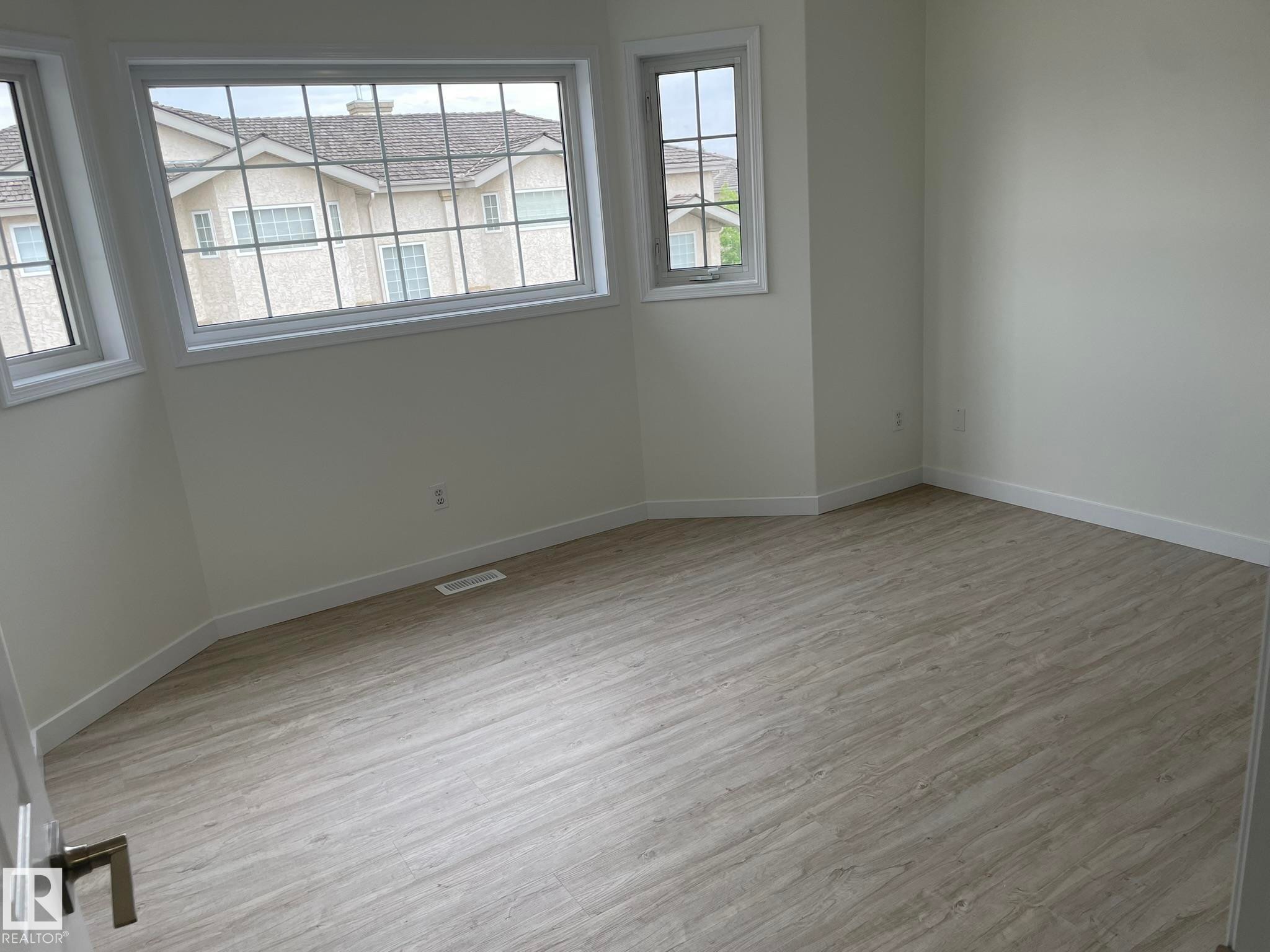 Spacious room featuring light wood-finish flooring, crisp white walls, and multiple windows with white trim - 2 1295 Carter Crest Road, Edmonton, AB - Indoor Photo Showing Other Room