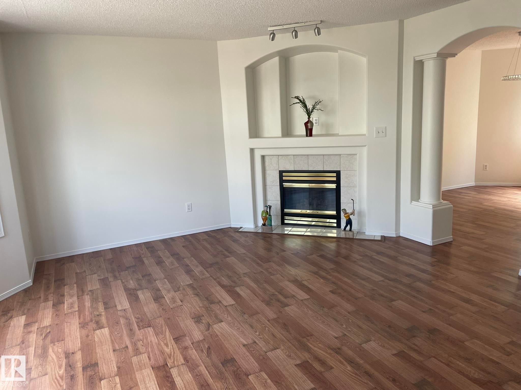 Living area featuring wood-finish flooring, a fireplace with a tile surround and mantel, built-in wall niches, and an arched entryway with decorative columns - 2 1295 Carter Crest Road, Edmonton, AB - Indoor Photo Showing Living Room With Fireplace
