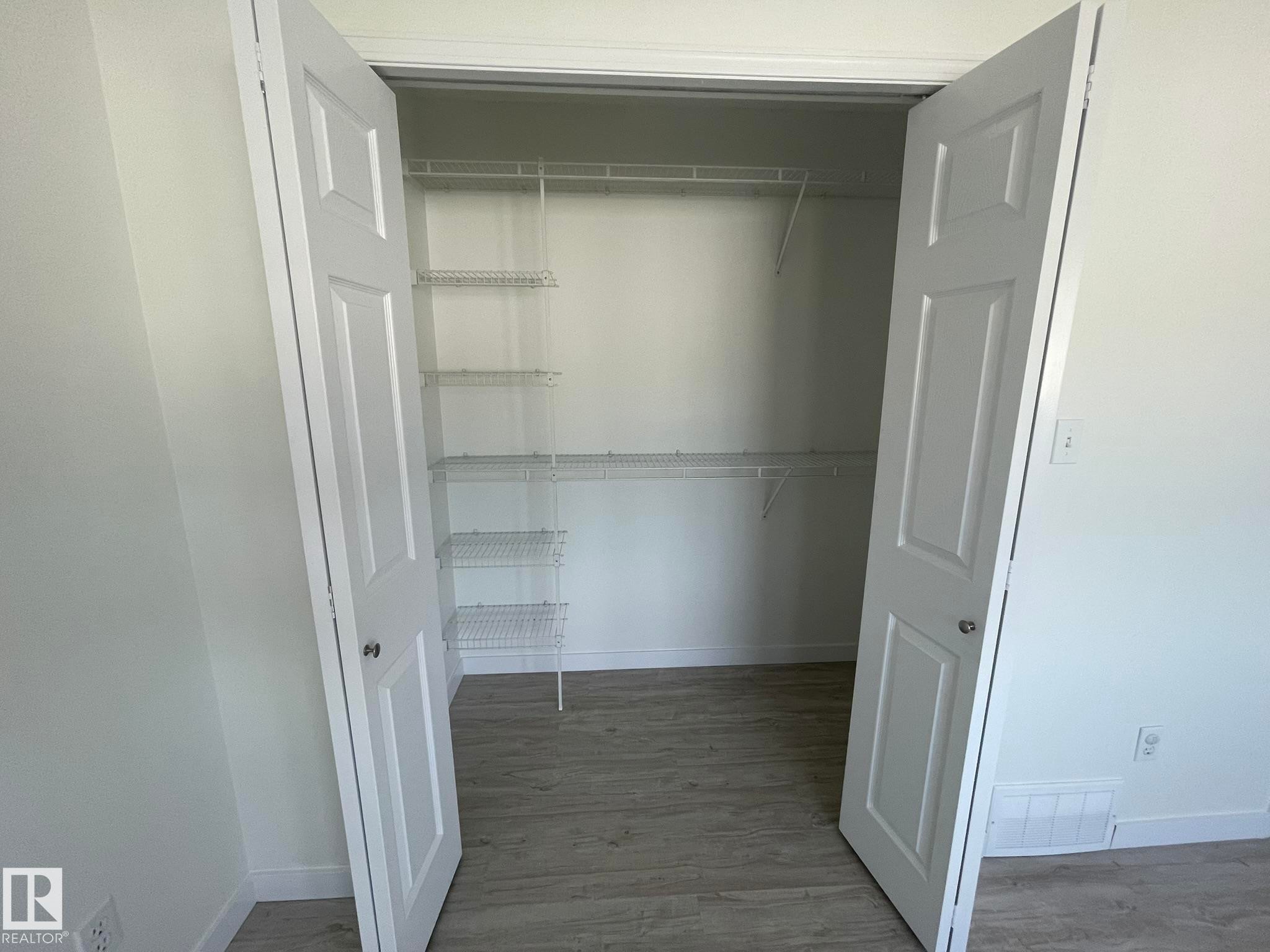Walk-in closet with double white paneled doors, wire shelving, and wood-finish flooring - 2 1295 Carter Crest Road, Edmonton, AB - Indoor With Storage