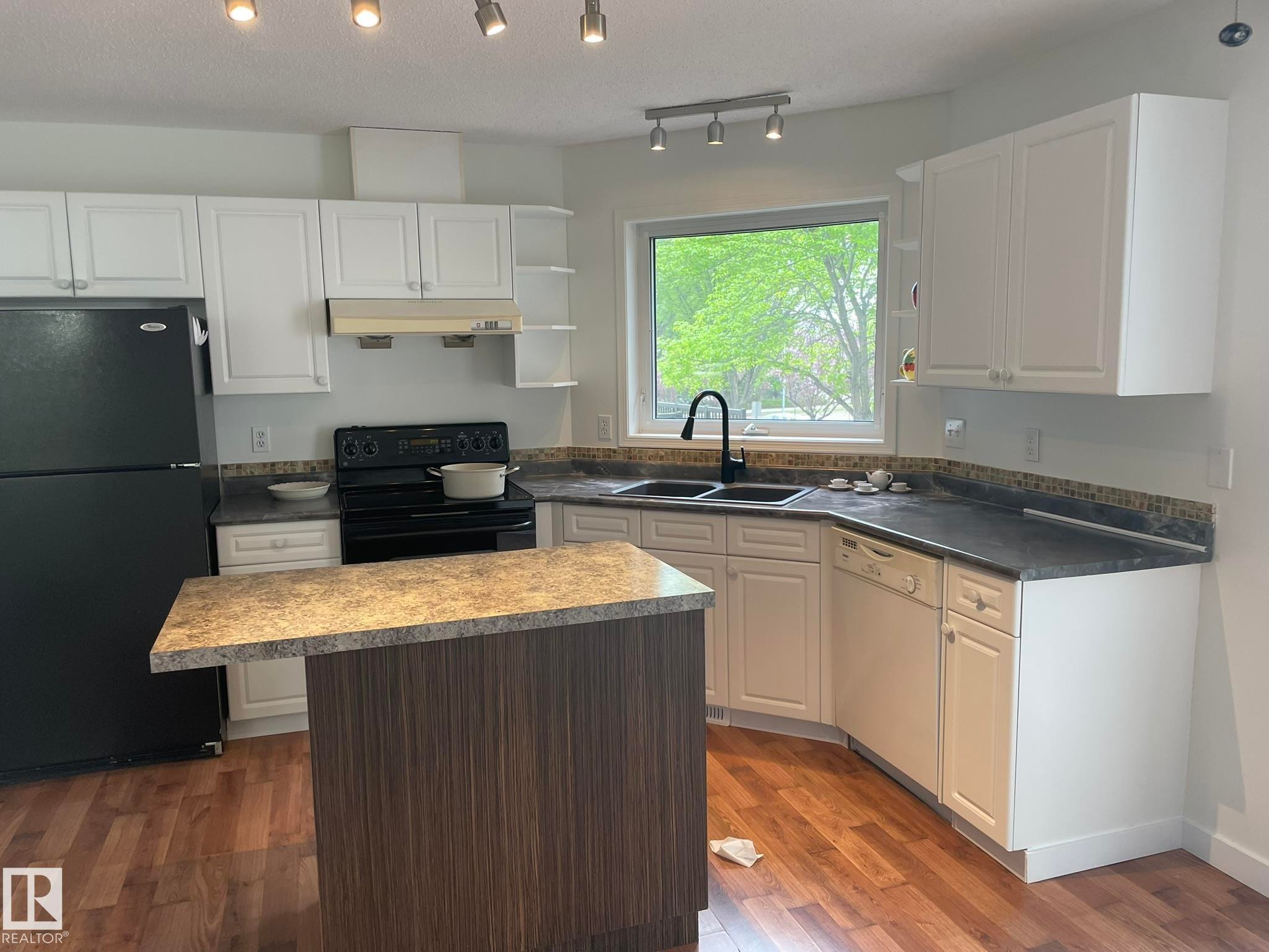 Kitchen featuring wood-finish flooring, white cabinetry, dark countertops, a black appliance suite, and a multi-purpose island with a contrasting wood-grain finish - 2 1295 Carter Crest Road, Edmonton, AB - Indoor Photo Showing Kitchen With Double Sink