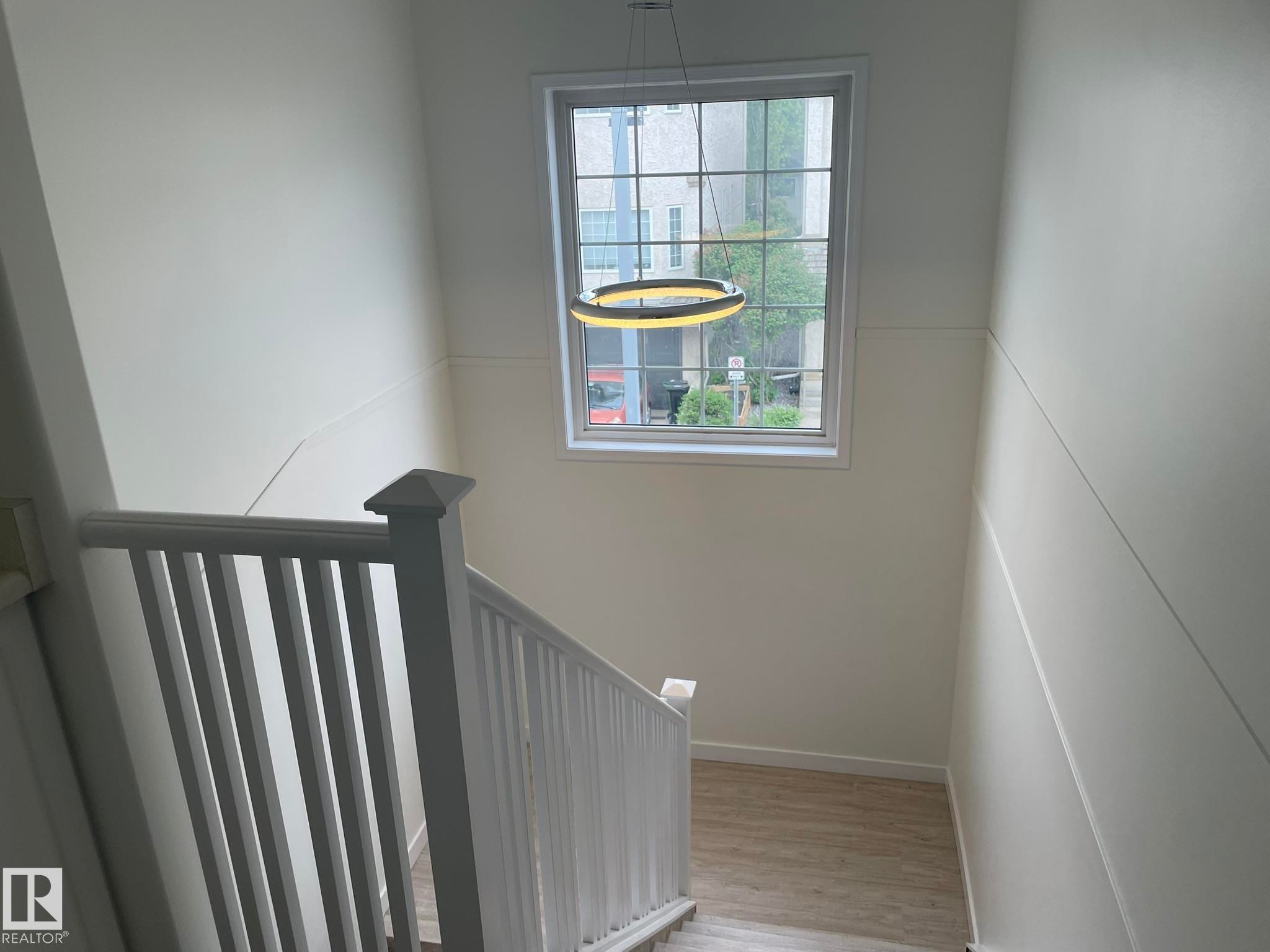 Staircase featuring wood-finish flooring, white banister with squared newel post, a large window with grid pattern, and a contemporary circular pendant light fixture - 2 1295 Carter Crest Road, Edmonton, AB - Indoor Photo Showing Other Room