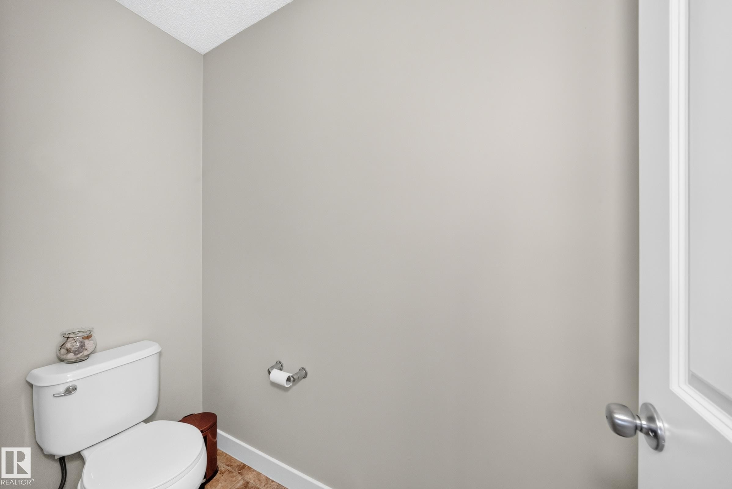 White porcelain toilet with a chrome flush lever, set against neutral-toned walls - 3433 Goodridge Link Link, Edmonton, AB