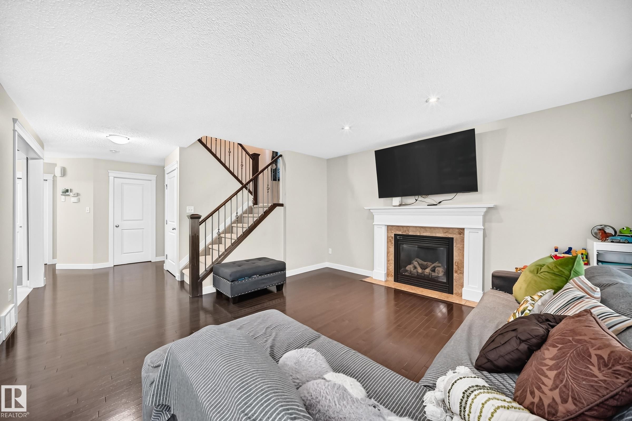 Living space featuring wood-finish flooring, a fireplace with a white mantel and stone surround, and recessed lighting - 3433 Goodridge Link Link, Edmonton, AB