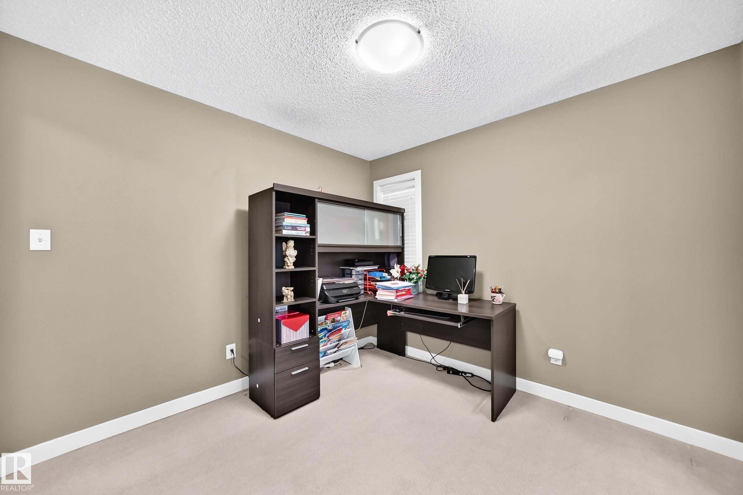 Neutral-toned room featuring a textured white ceiling, light carpeting, and a built-in office desk with accompanying shelving - 3433 Goodridge Link Link, Edmonton, AB