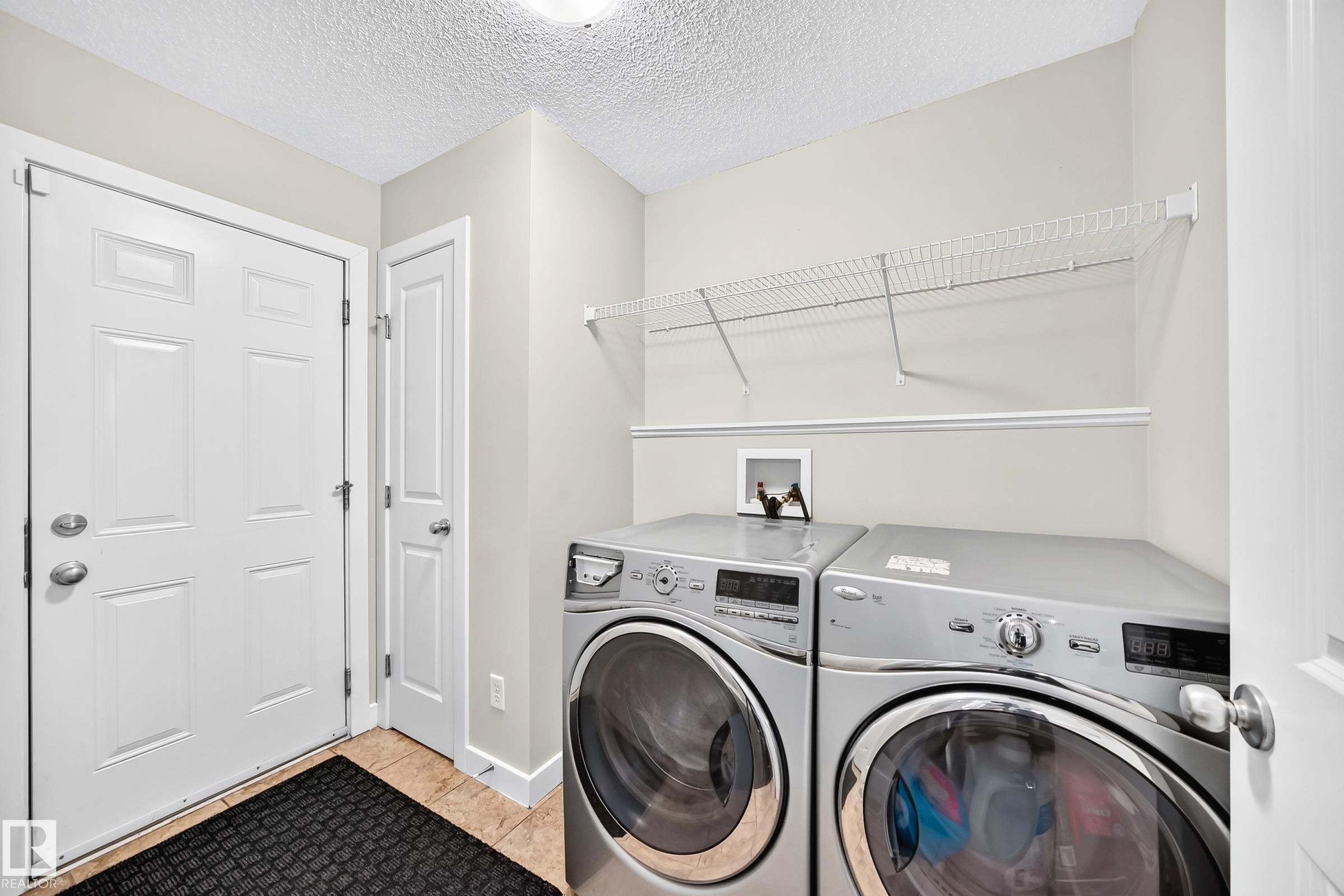 Dedicated laundry area featuring a tile floor, white panel doors, and overhead wire shelving - 3433 Goodridge Link Link, Edmonton, AB