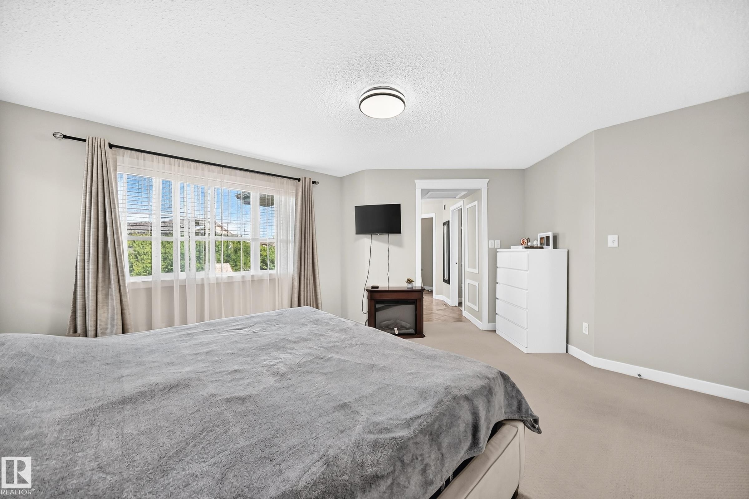 Spacious bedroom with a large window, neutral wall tones, white trim, and a ceiling-mounted light fixture - 3433 Goodridge Link Link, Edmonton, AB
