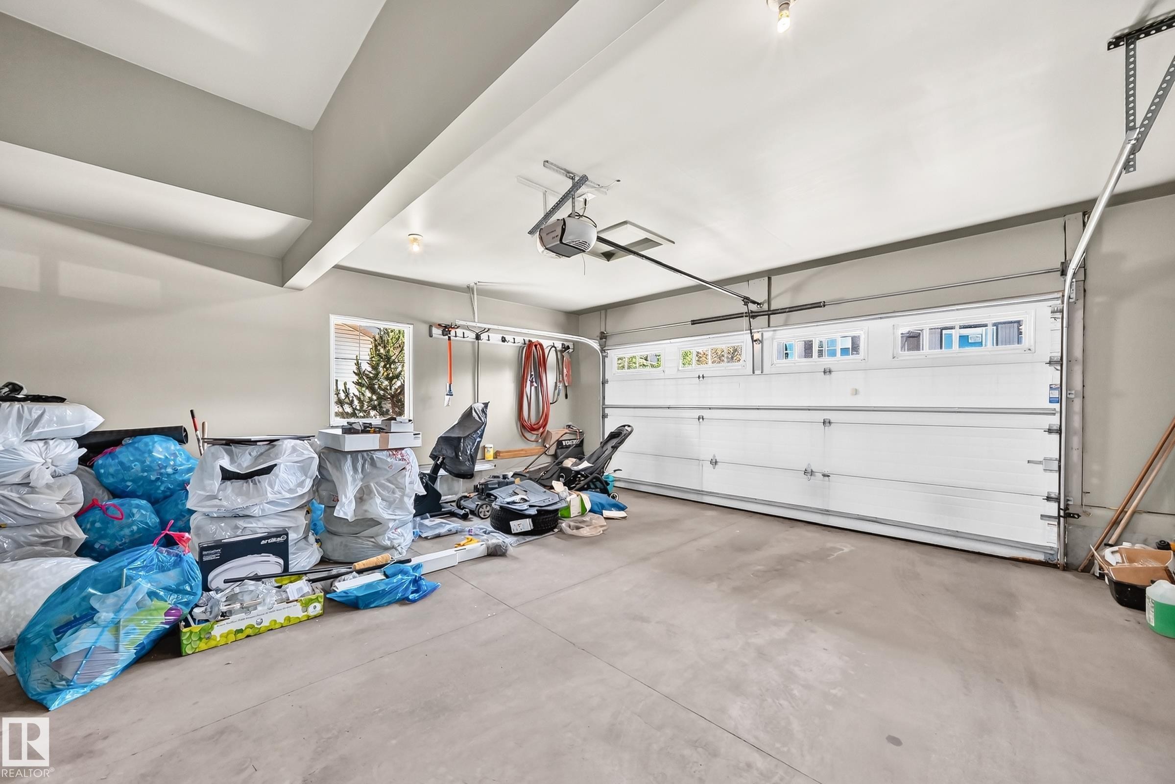 Spacious garage featuring a concrete floor, light gray walls, and an overhead garage door with upper window inserts - 3433 Goodridge Link Link, Edmonton, AB
