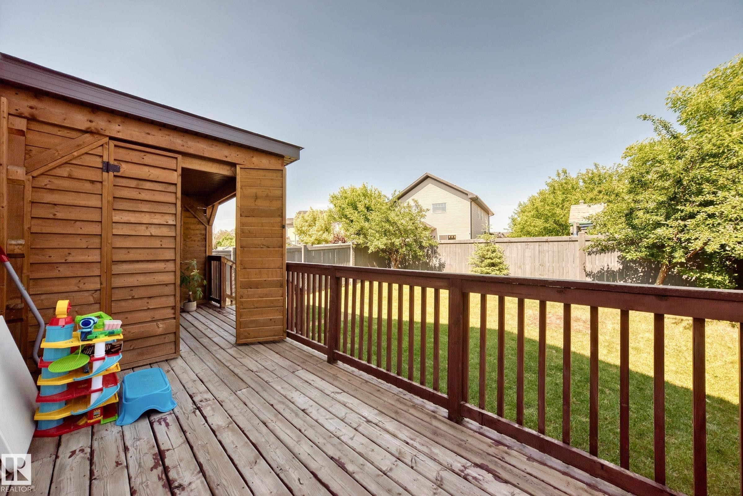 Expansive wood deck with a built-in storage shed, featuring a dark wood railing and a spacious green lawn - 3433 Goodridge Link Link, Edmonton, AB