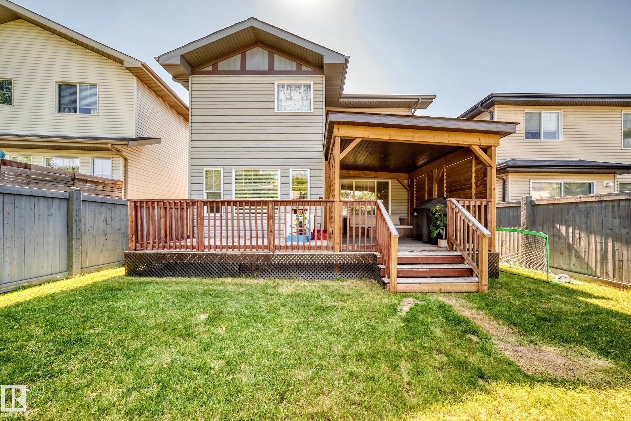 Expansive backyard with a covered wooden deck, privacy fencing, and a manicured lawn - 3433 Goodridge Link Link, Edmonton, AB