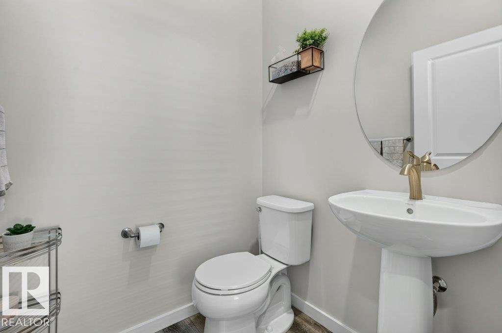 Pedestal sink with a gold-tone faucet, round wall mirror, and wood-finish flooring - 2116 Maple Road, Edmonton, AB