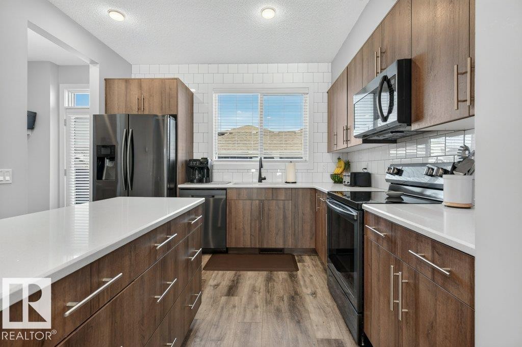 Contemporary kitchen featuring wood-finish cabinetry, white countertops, and a subway tile backsplash - 2116 Maple Road, Edmonton, AB