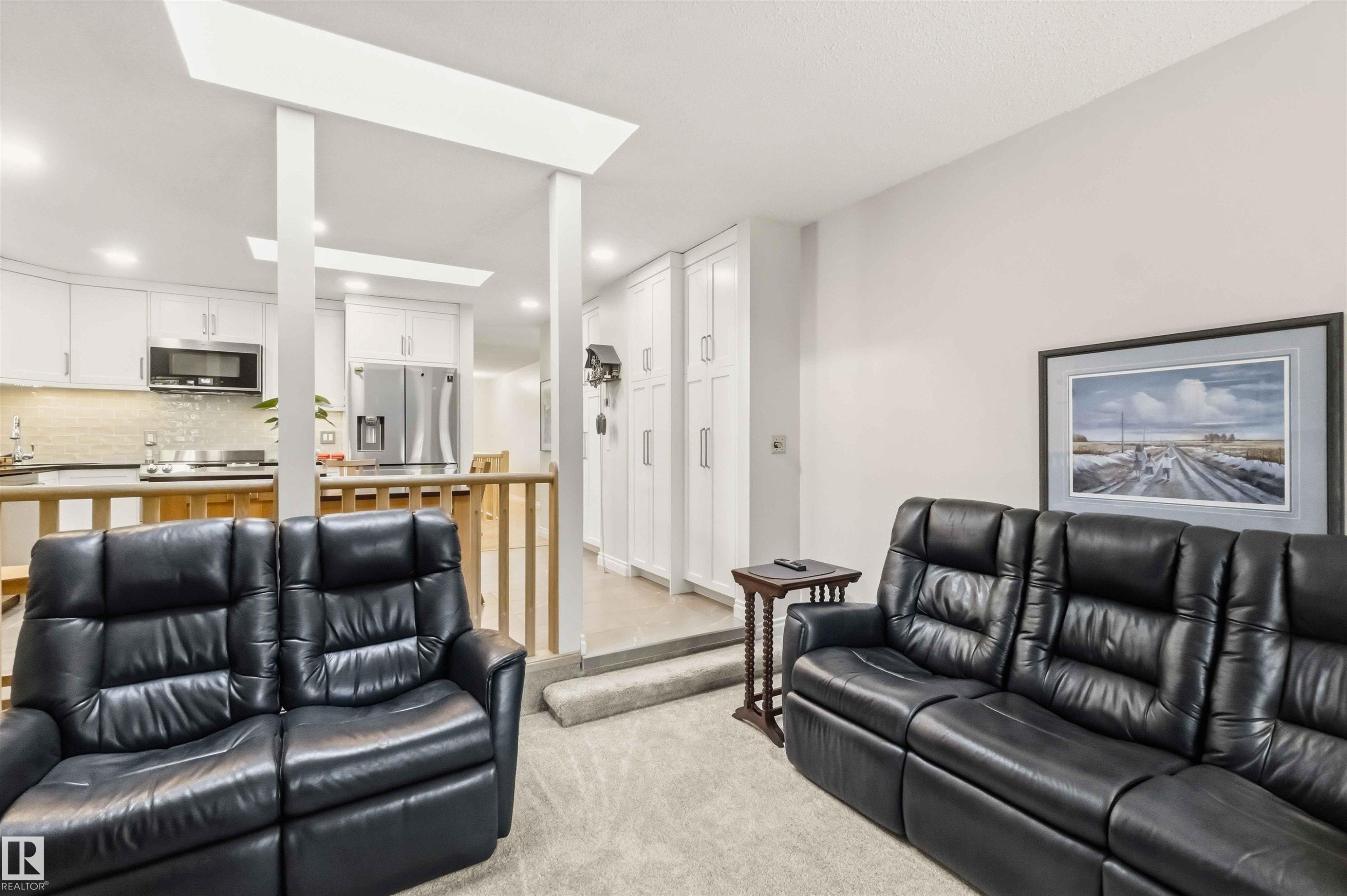 Carpeted living area featuring a vaulted ceiling and a partial wall separating it from a kitchen with stainless steel appliances, a tile backsplash, and light-toned cabinetry - 31 Gariepy Crescent, Edmonton, AB