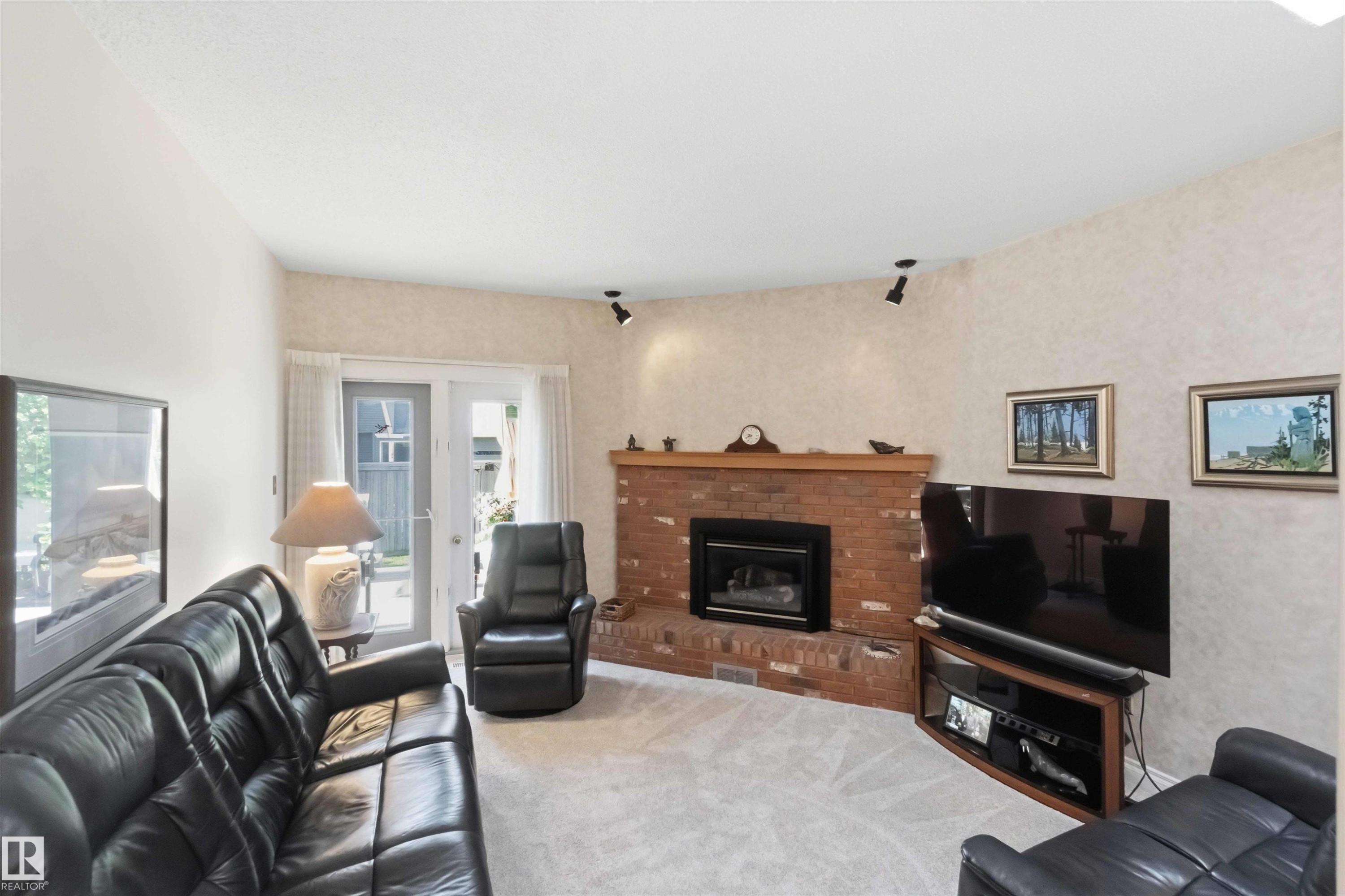 Living area featuring a brick fireplace with a wood mantle, neutral carpeting, and track lighting - 31 Gariepy Crescent, Edmonton, AB