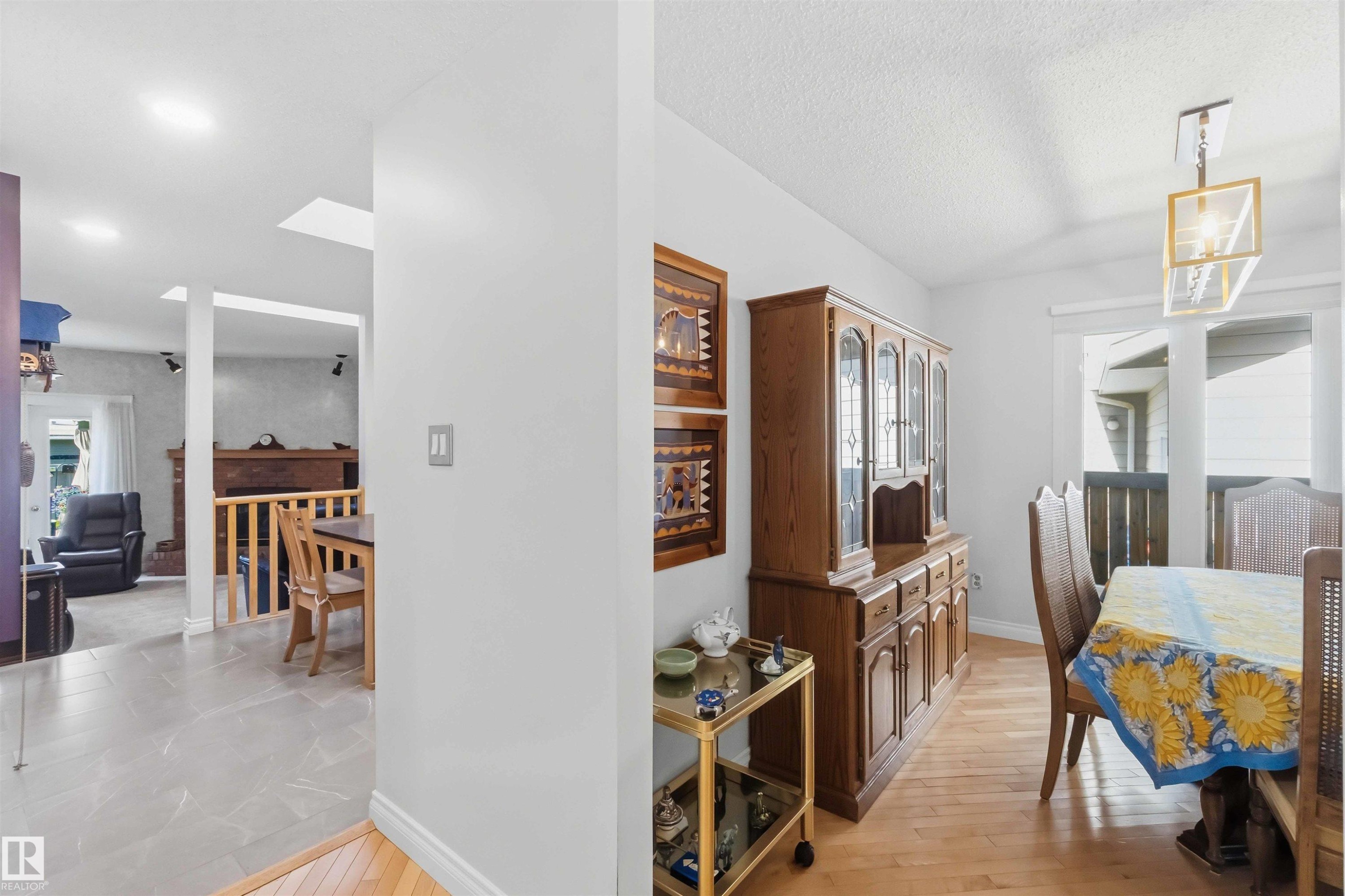 Bright dining area featuring wood-finish flooring, a contemporary linear chandelier, and ample natural light from exterior windows - 31 Gariepy Crescent, Edmonton, AB