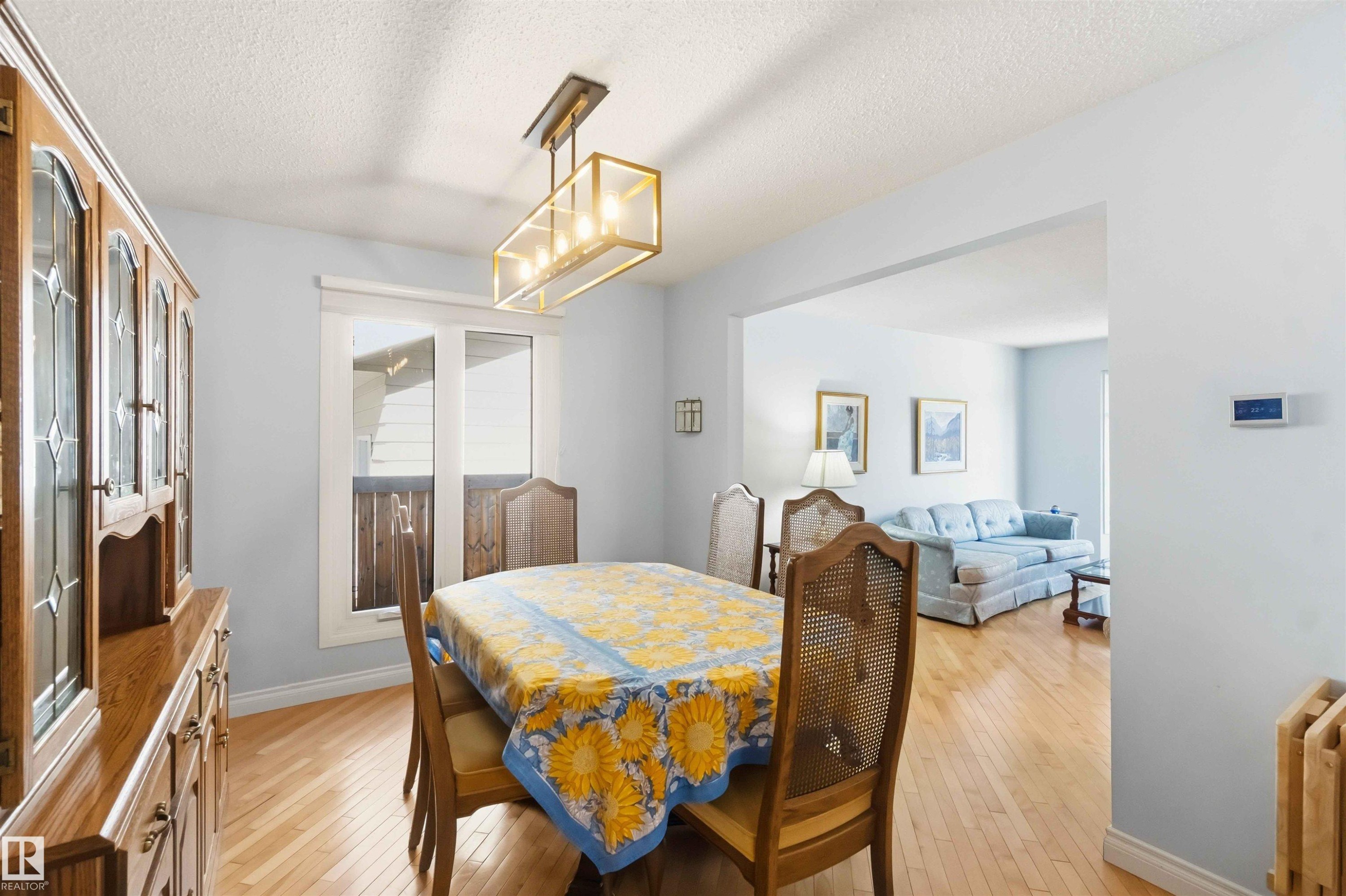 Dining area with light wood-finish flooring, a contemporary linear chandelier, and a large window - 31 Gariepy Crescent, Edmonton, AB