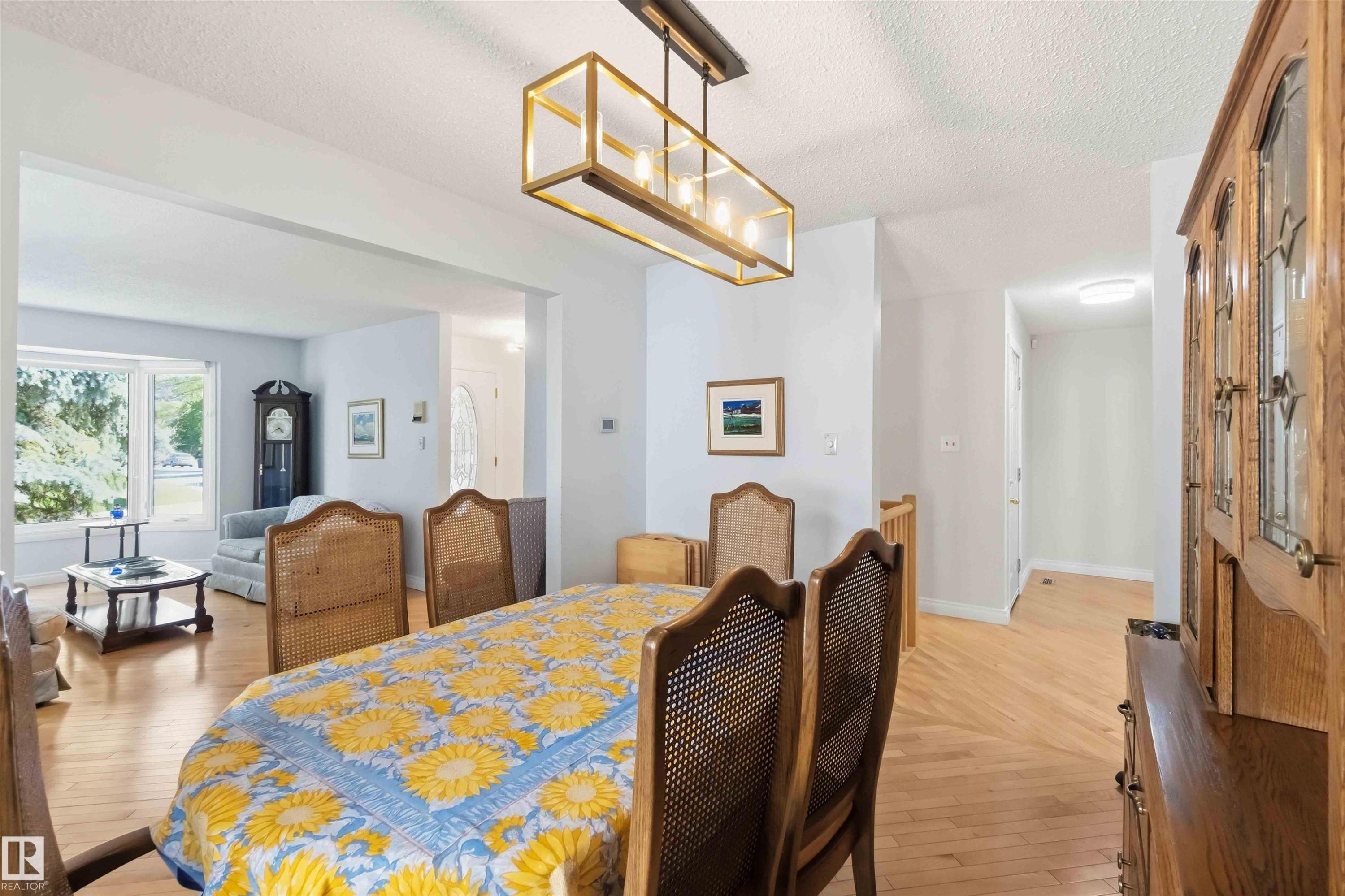 Dining area with wood-finish flooring featuring a herringbone pattern, illuminated by a rectangular brass-tone chandelier - 31 Gariepy Crescent, Edmonton, AB