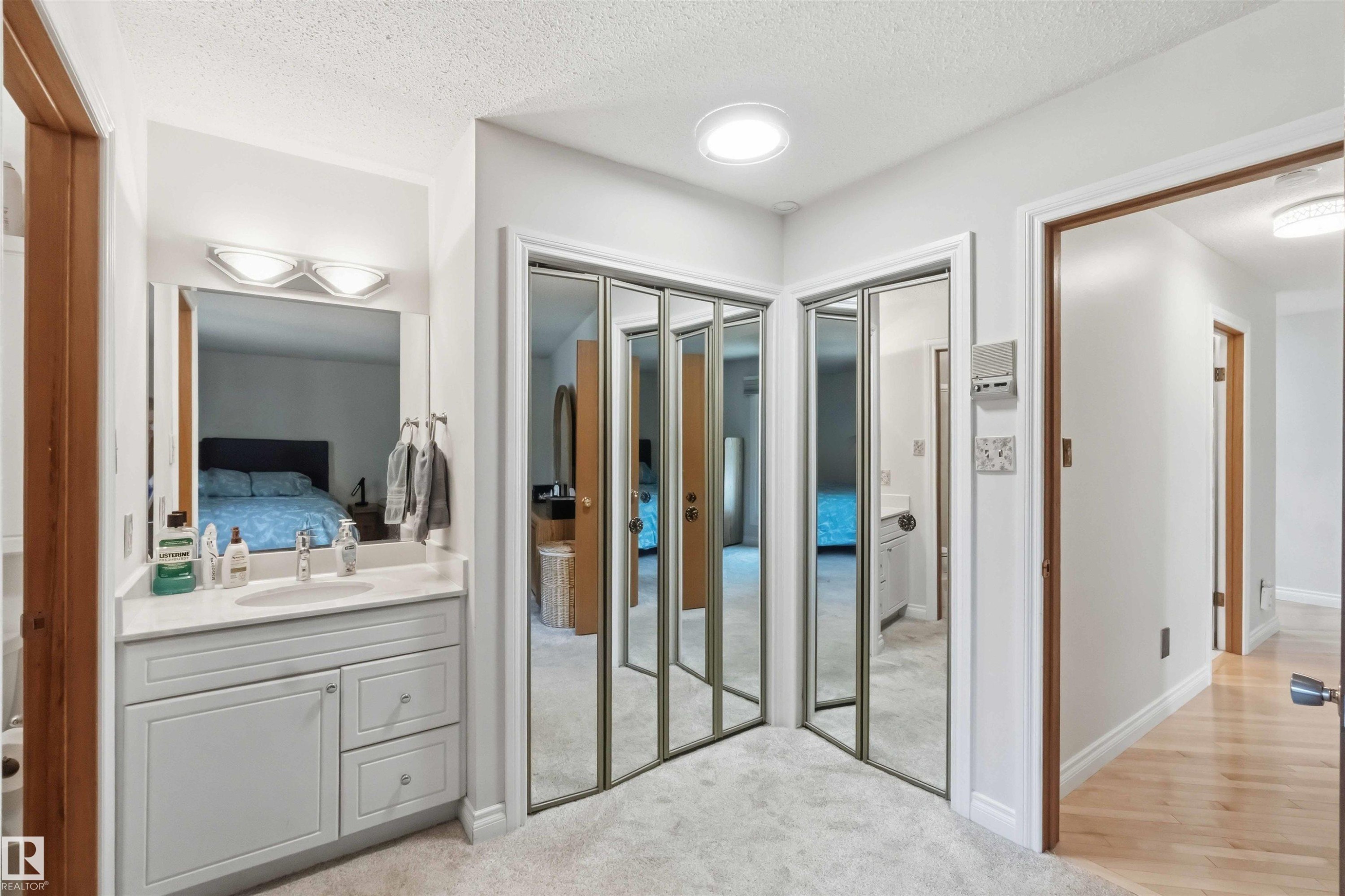 Hallway featuring a built-in vanity with a rectangular sink, a white countertop, and mirrored bi-fold closet doors - 31 Gariepy Crescent, Edmonton, AB