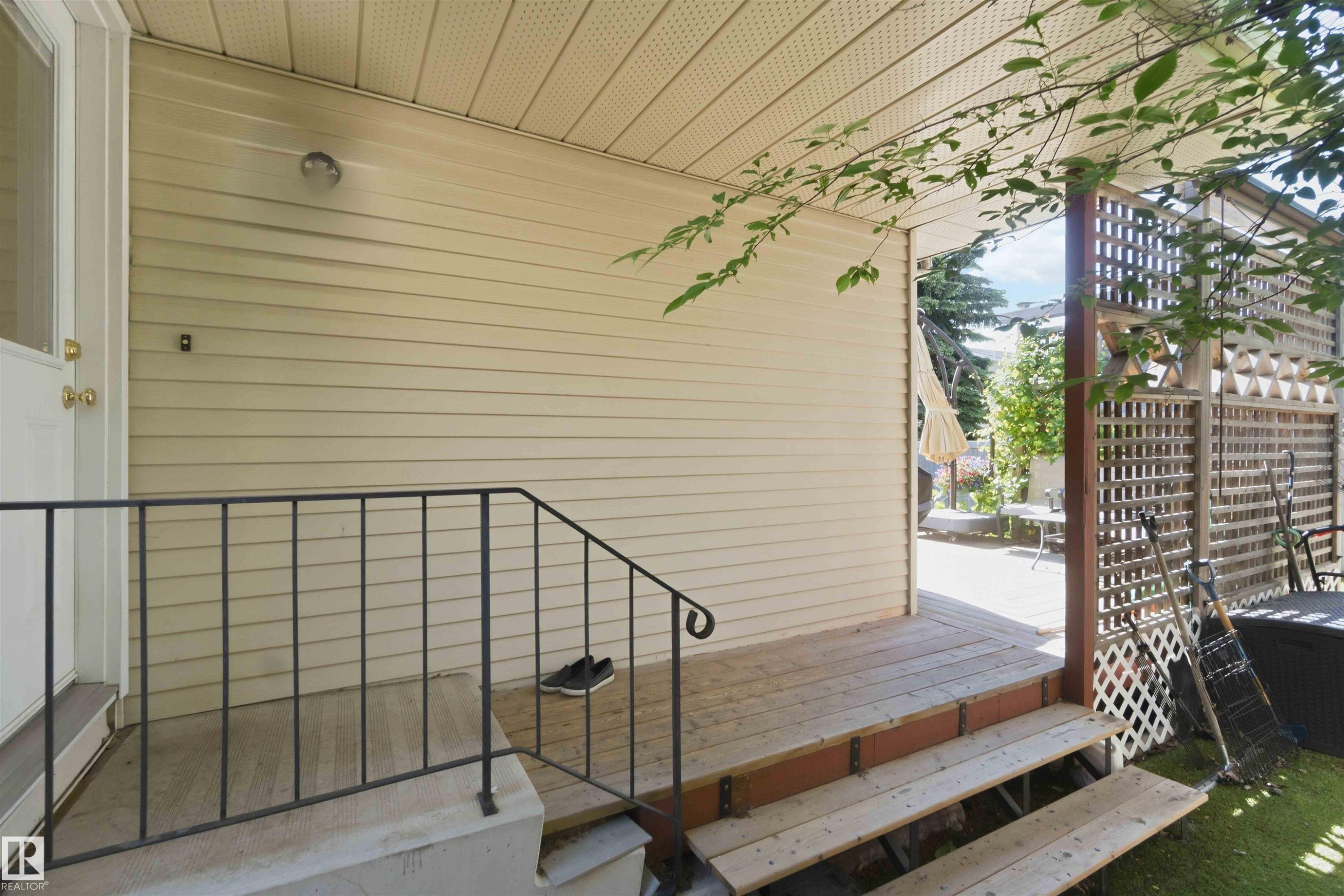 Exterior entrance featuring a wood-finish porch, black metal railing, cream-colored siding, and a lattice privacy screen - 31 Gariepy Crescent, Edmonton, AB