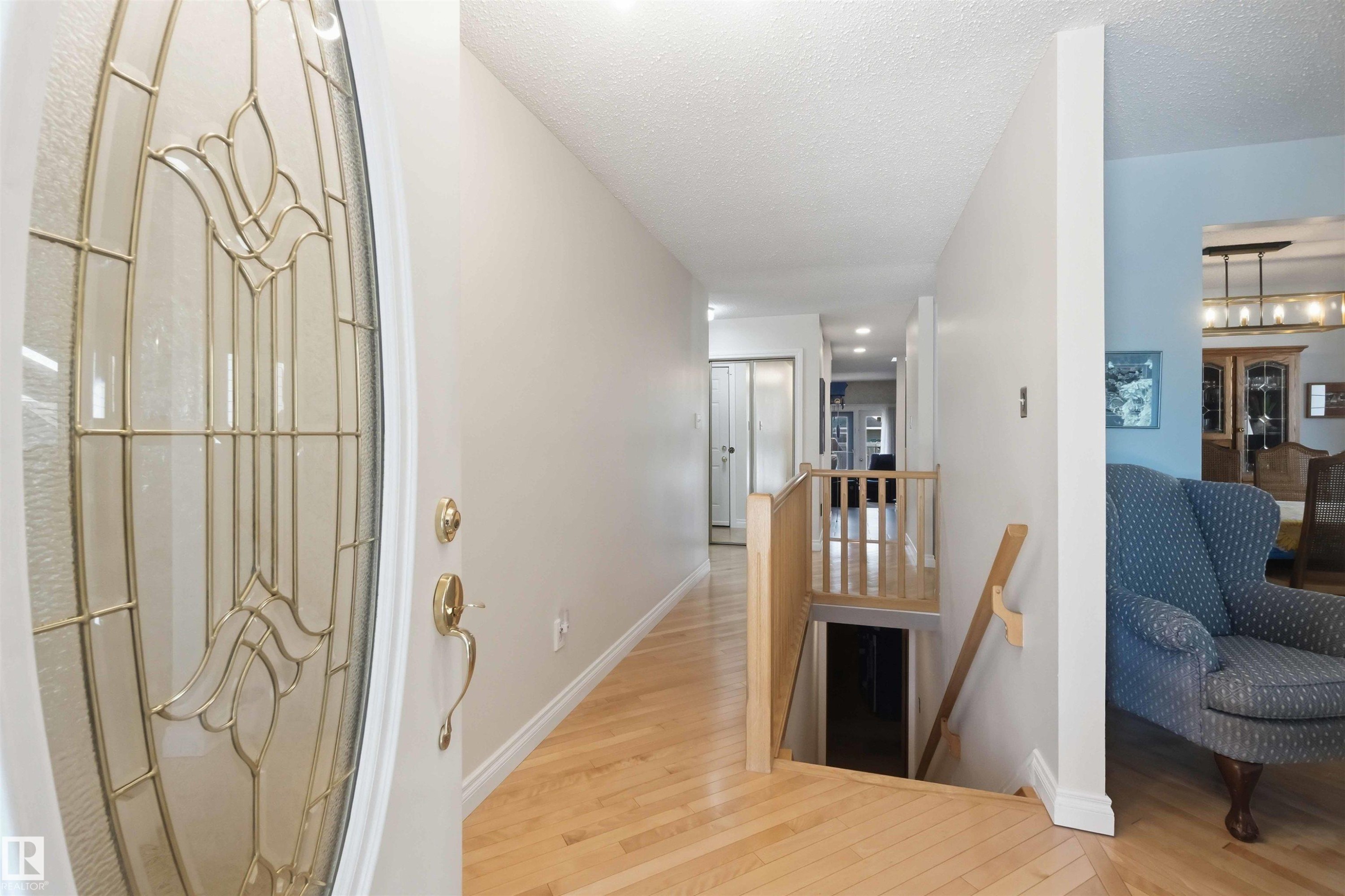 Entryway featuring a decorative glass door with brass hardware, light wood-finish flooring, and a wooden handrail leading to a lower level - 31 Gariepy Crescent, Edmonton, AB
