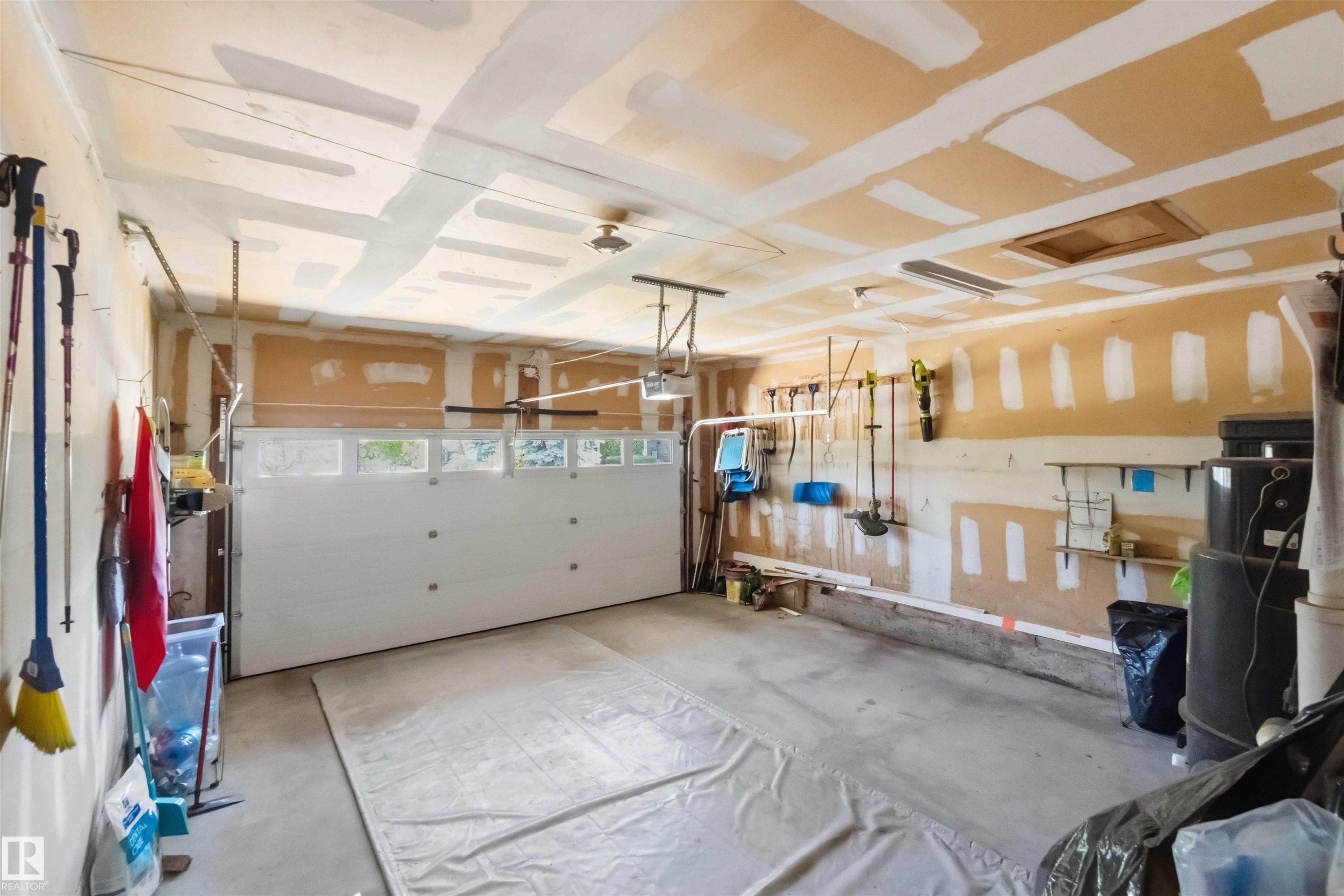 Attached garage featuring a white overhead door with transom-style windows, concrete flooring, and an exposed ceiling - 31 Gariepy Crescent, Edmonton, AB