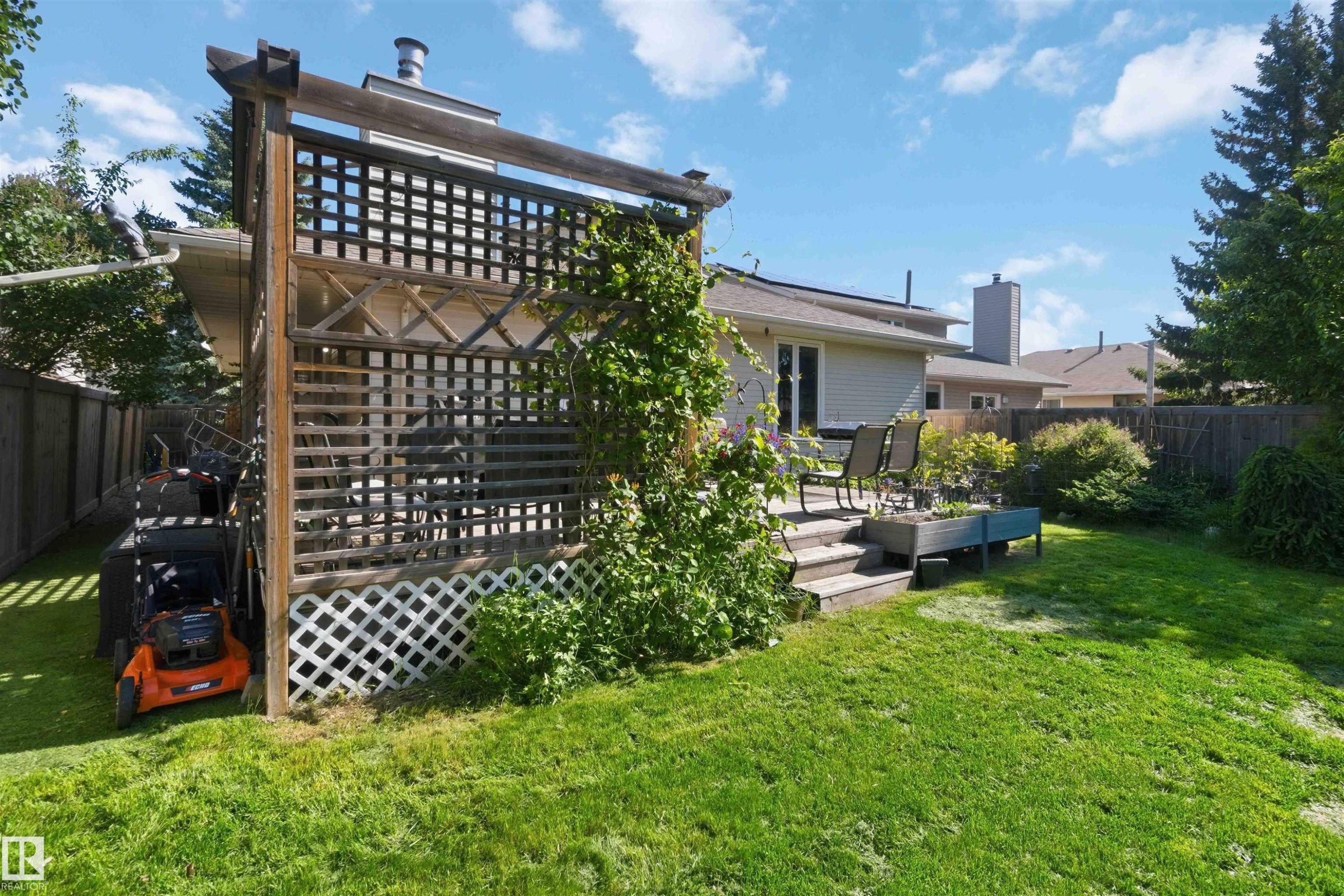 Spacious backyard featuring a wooden deck with steps, a wood lattice privacy screen, a raised garden planter, and a generously sized lawn area - 31 Gariepy Crescent, Edmonton, AB