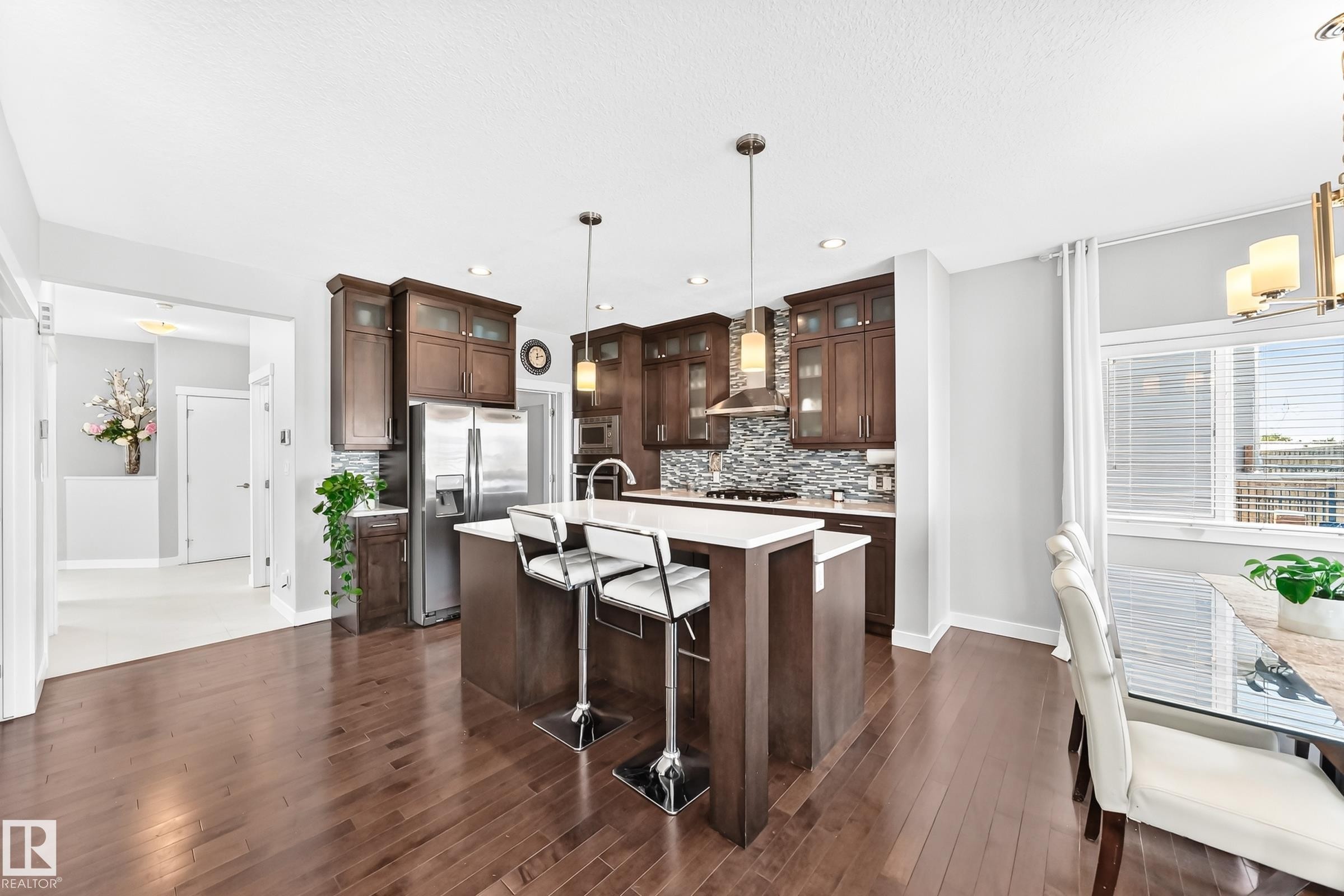 Kitchen featuring a central island with white countertop, dark wood-finish cabinetry, stainless steel appliances, and a tiled backsplash - 3672 Claxton Place Sw, Edmonton, AB
