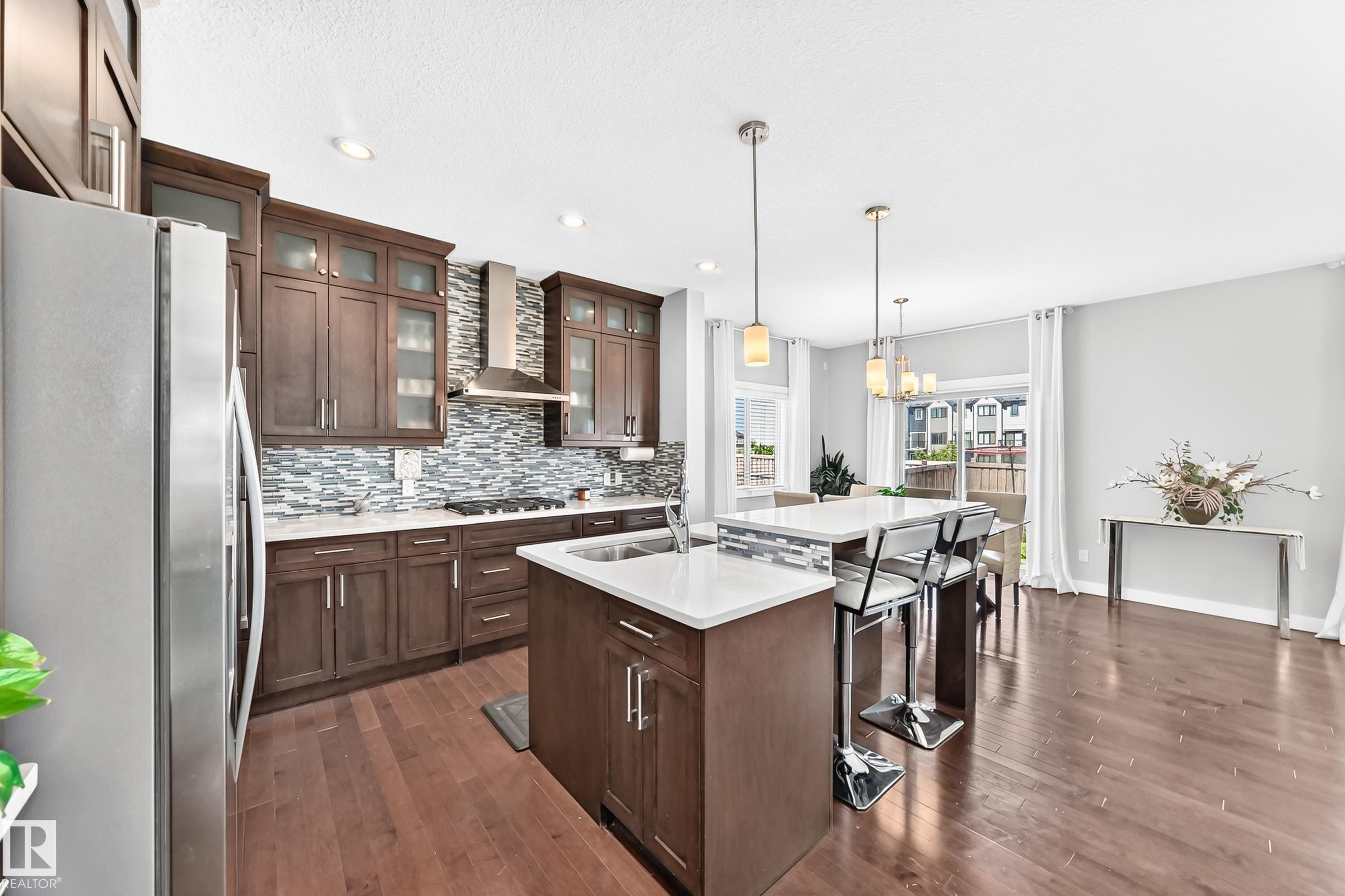 Open-concept kitchen featuring wood-finish flooring, dark wood cabinetry, white countertops, and a full-height tile backsplash - 3672 Claxton Place Sw, Edmonton, AB