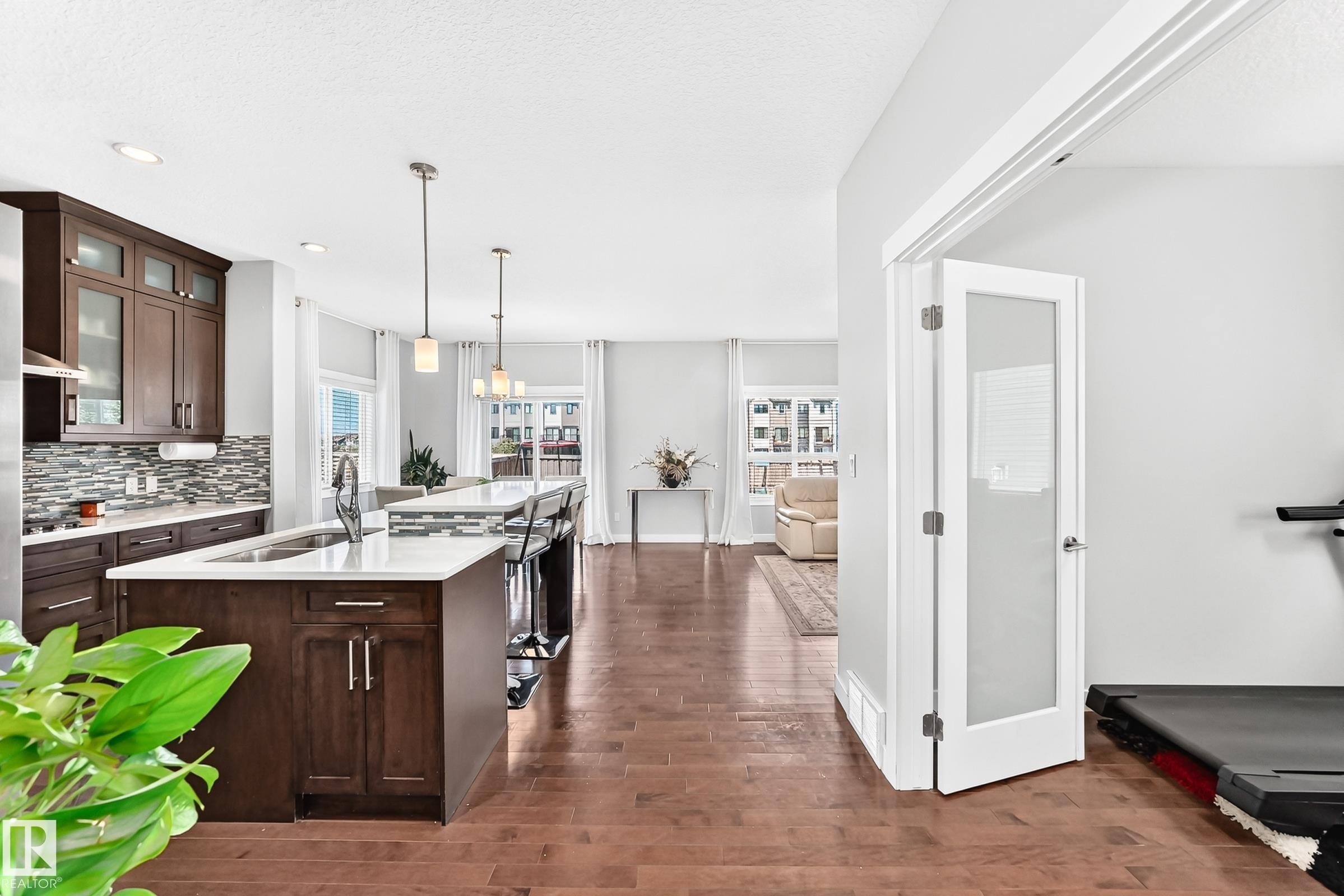Modern kitchen featuring dark wood cabinetry, white countertops, a mosaic tile backsplash, and a large island with pendant lighting - 3672 Claxton Place Sw, Edmonton, AB