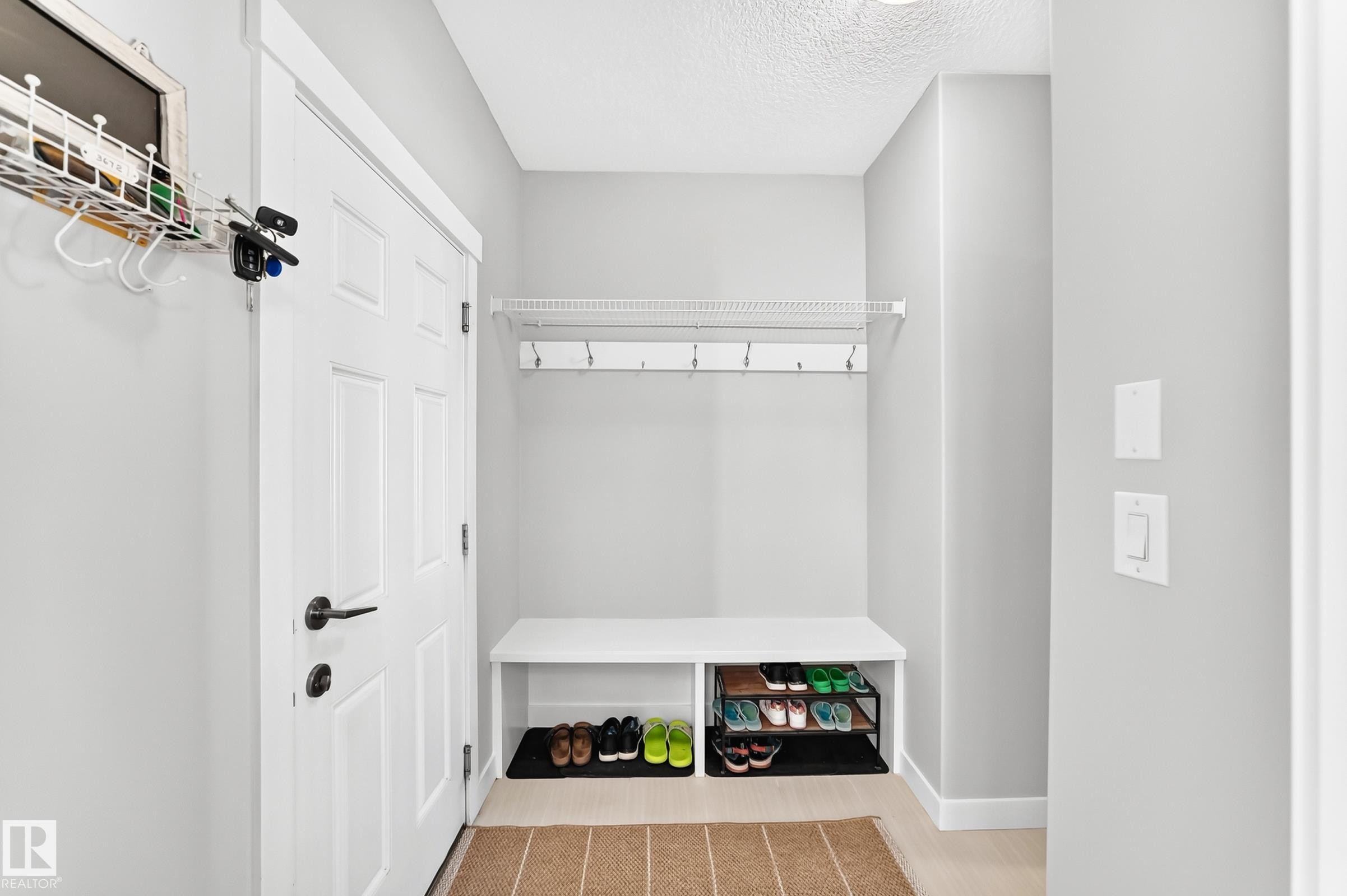 Entryway featuring a white paneled door, black hardware, light-toned flooring, built-in bench seating, and wall-mounted shelving with hooks - 3672 Claxton Place Sw, Edmonton, AB