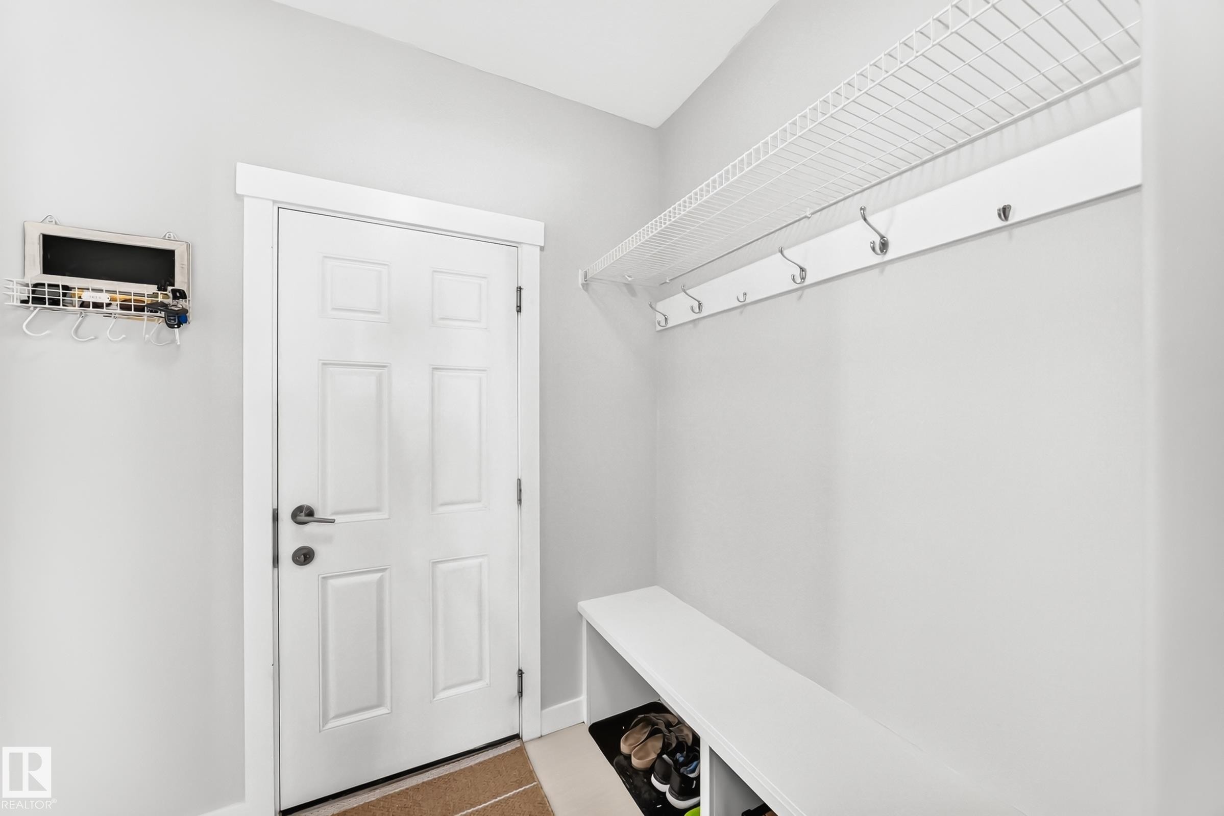 Entryway featuring a six-panel door, built-in bench, and wall-mounted storage with hooks and shelving - 3672 Claxton Place Sw, Edmonton, AB