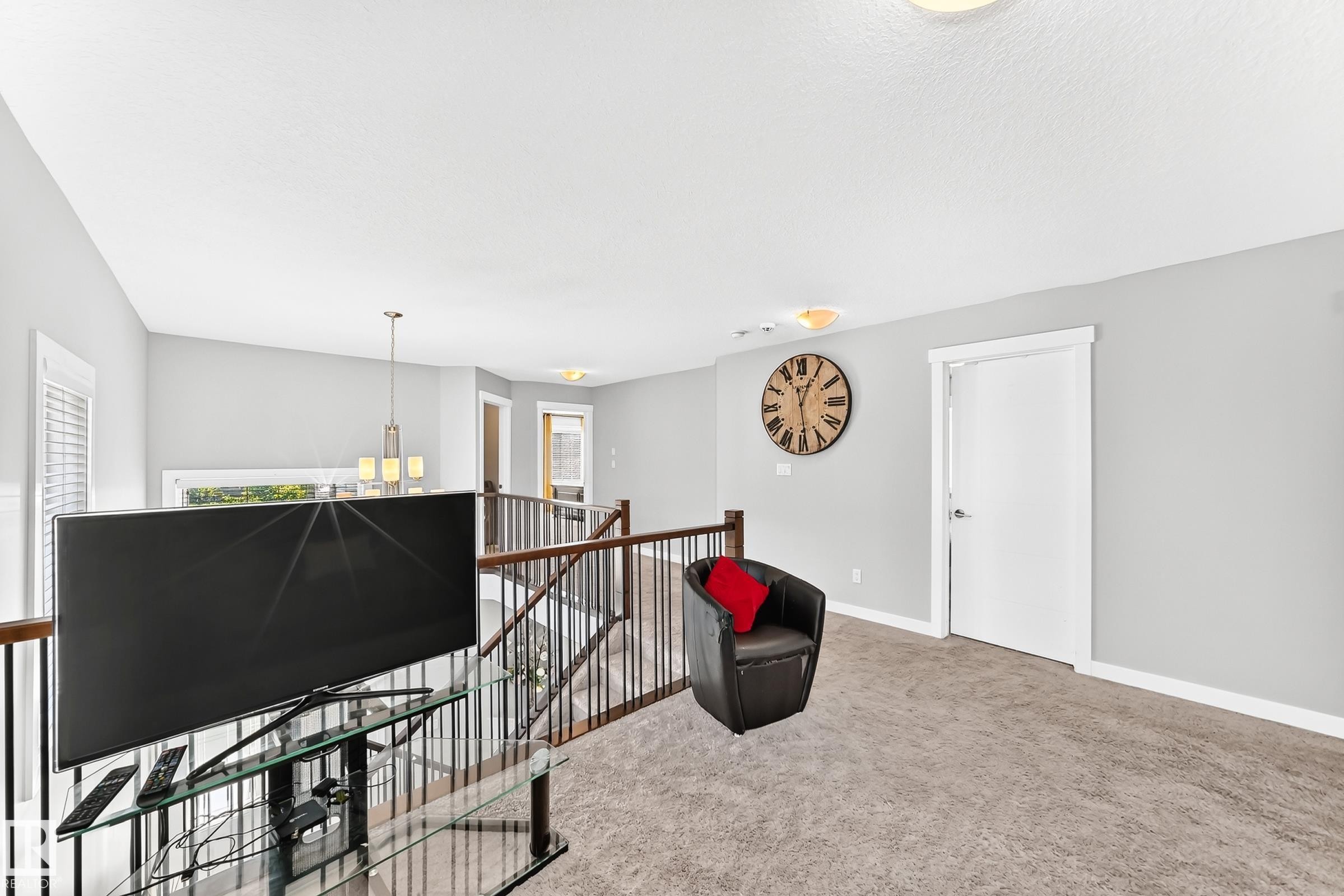 Carpeted loft area featuring a white door, light grey walls, and a wood-finish railing with black spindles - 3672 Claxton Place Sw, Edmonton, AB
