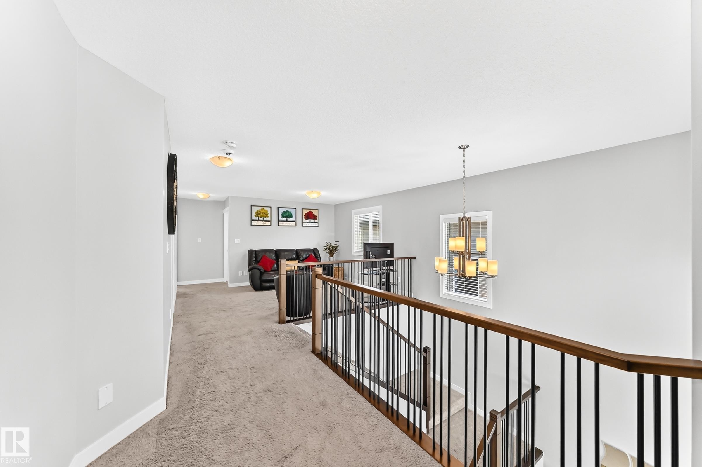 Upper level landing featuring carpeted flooring, wood-finish handrails with black balusters, and a contemporary chandelier - 3672 Claxton Place Sw, Edmonton, AB