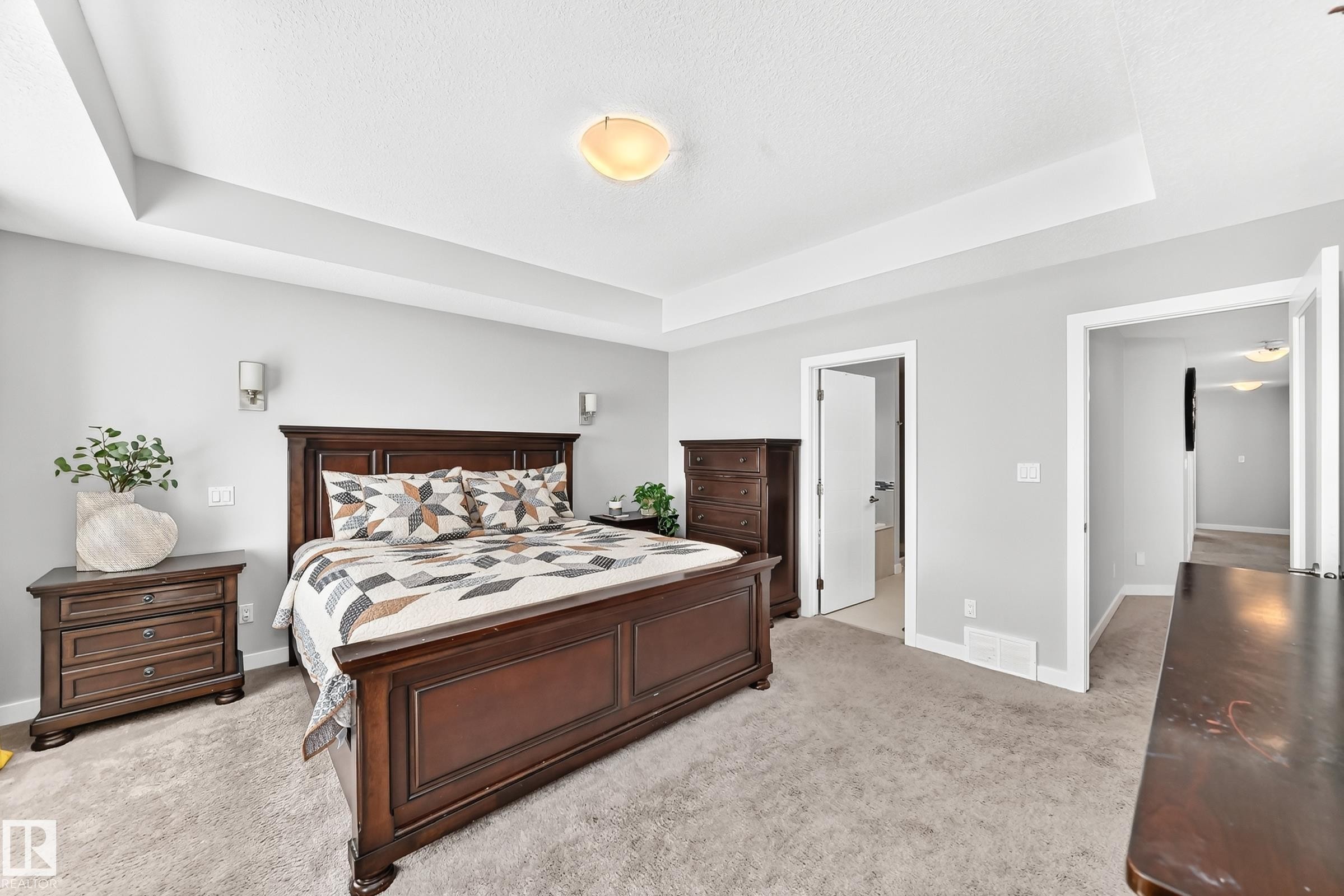 Spacious room featuring tray ceiling, light gray walls, wall sconces, ceiling light fixture, and plush carpeting - 3672 Claxton Place Sw, Edmonton, AB