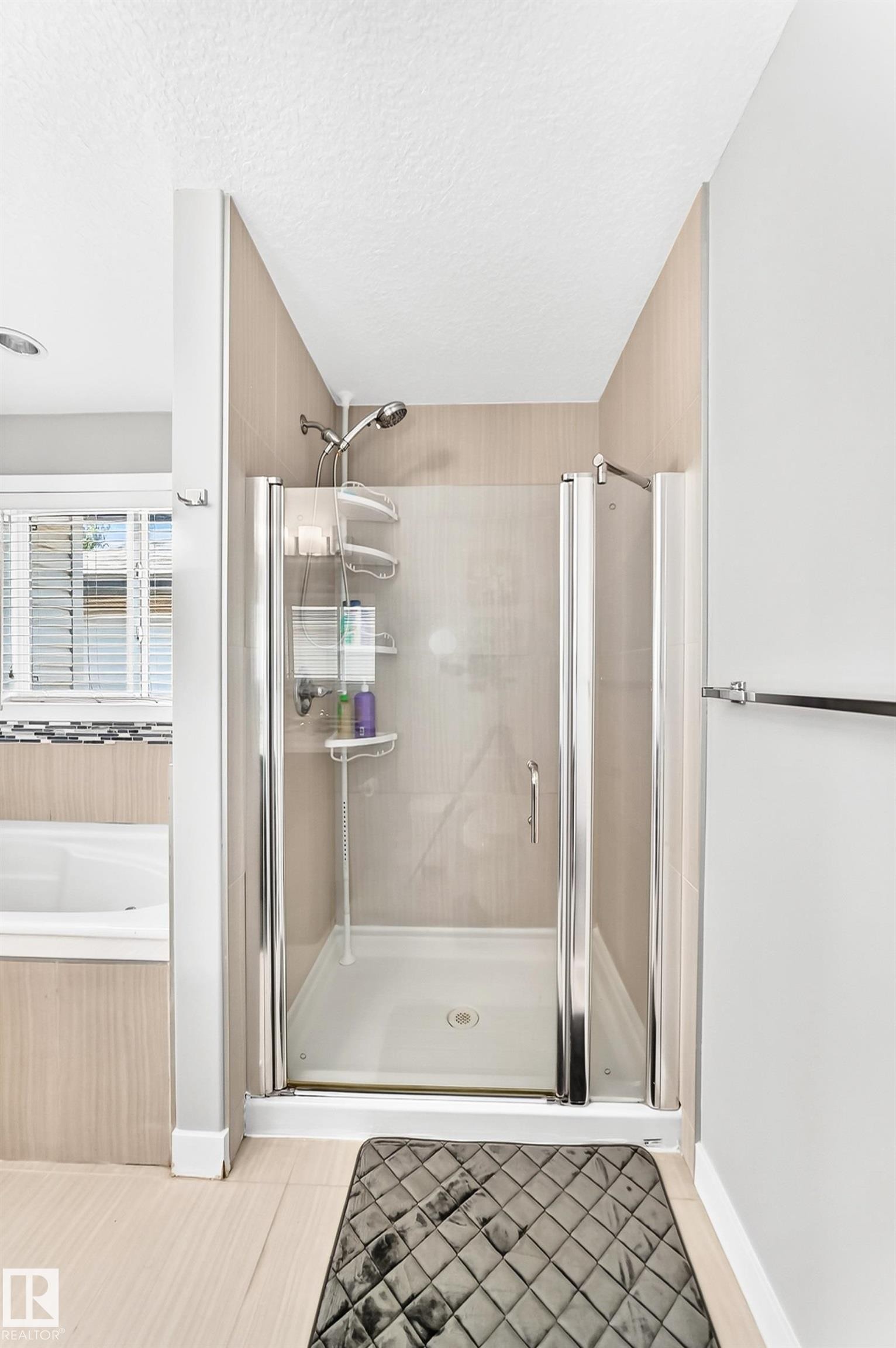 Glass-enclosed shower with a handheld showerhead and built-in shelving, complemented by a soaking tub with tile surround and a privacy window with blinds - 3672 Claxton Place Sw, Edmonton, AB
