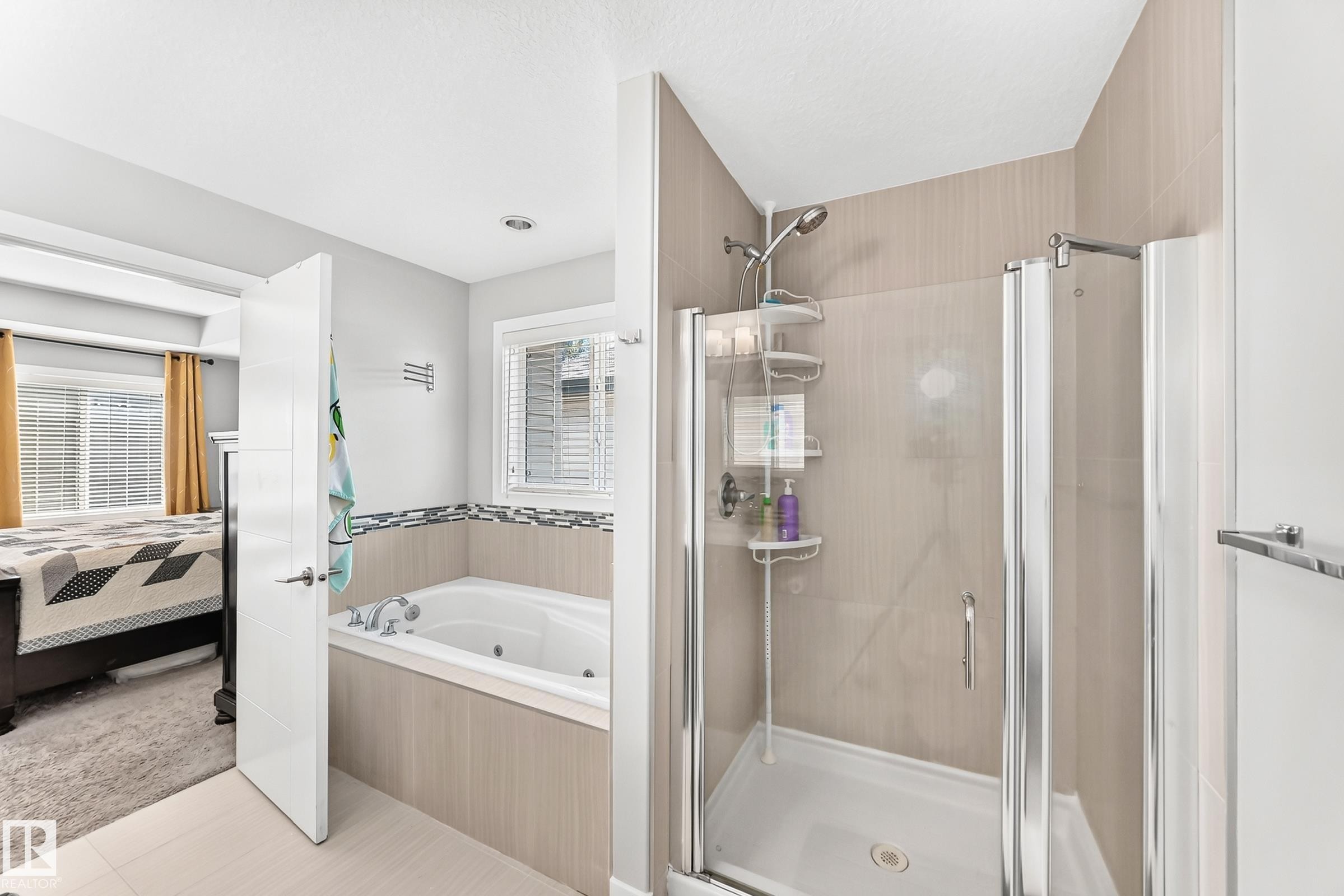 Bathroom featuring a built-in jetted tub with tile surround, a separate glass-enclosed shower, light grey wall paint, and a large window with horizontal blinds - 3672 Claxton Place Sw, Edmonton, AB