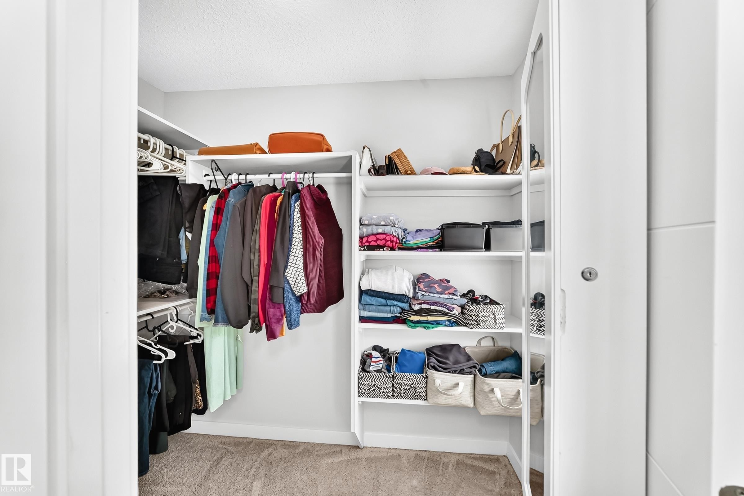 Walk-in closet featuring white built-in shelving, multiple hanging rods, and a neutral carpeted floor - 3672 Claxton Place Sw, Edmonton, AB