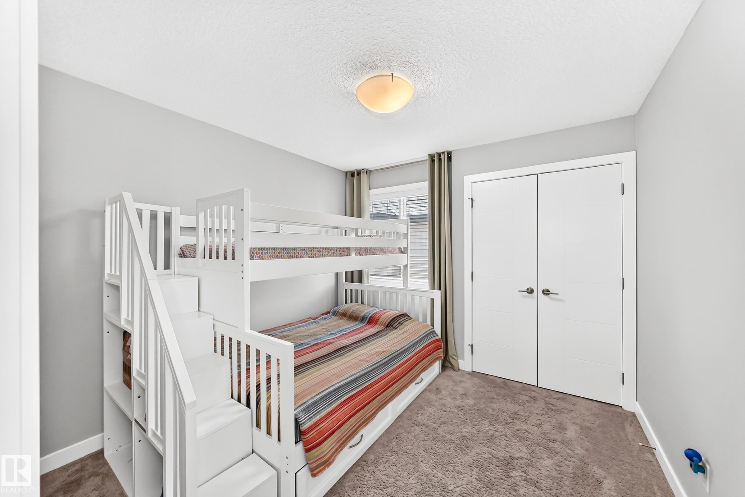 Room featuring light gray walls, textured carpet flooring, a flush-mount ceiling light, and white bi-fold closet doors with brushed nickel hardware - 3672 Claxton Place Sw, Edmonton, AB