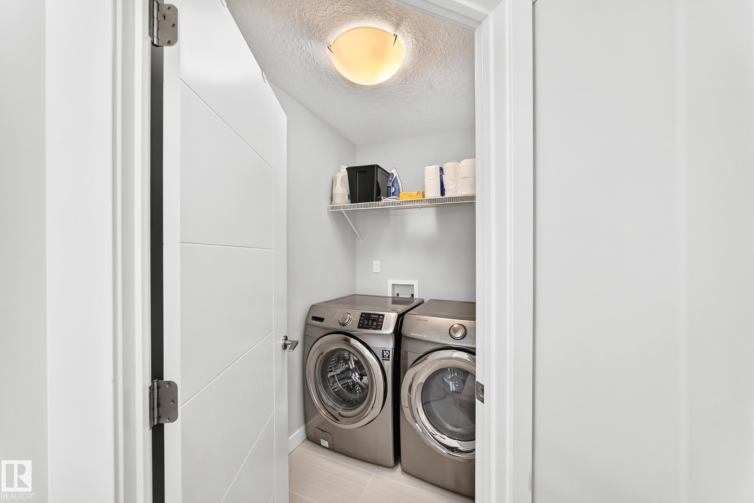 Dedicated laundry area featuring a front-loading washer and dryer set, wire shelving, and overhead lighting - 3672 Claxton Place Sw, Edmonton, AB