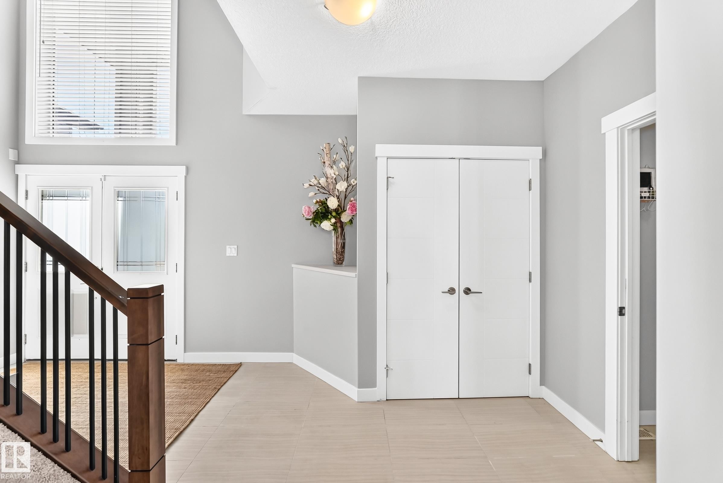 Foyer featuring light plank flooring, a dark wood-finish staircase with black spindles, a double-door entry with frosted glass, white trim, and a high window with blinds - 3672 Claxton Place Sw, Edmonton, AB