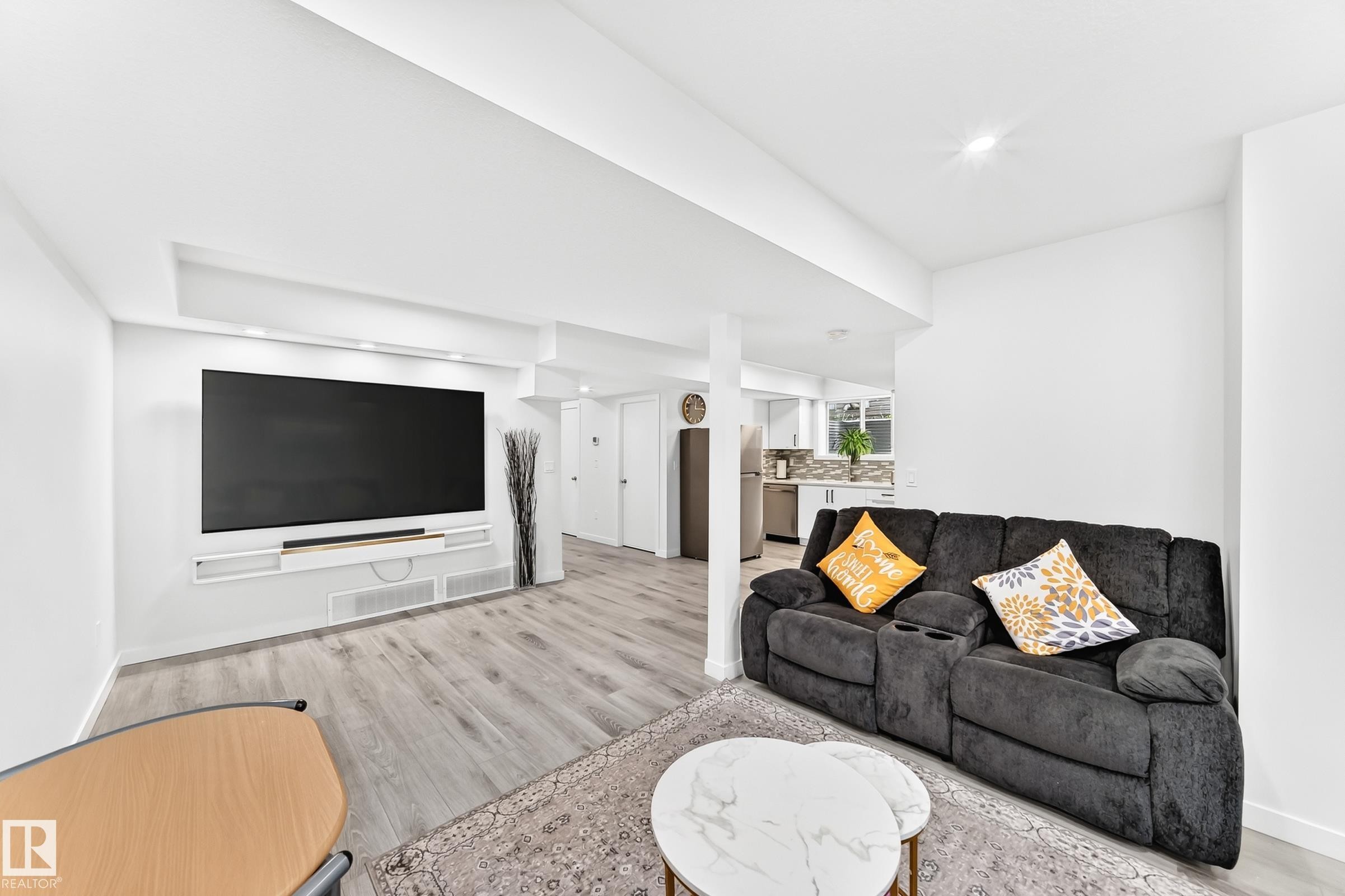Open-concept living area with light wood-finish flooring, a built-in media console, recessed lighting, and a white color palette - 3672 Claxton Place Sw, Edmonton, AB