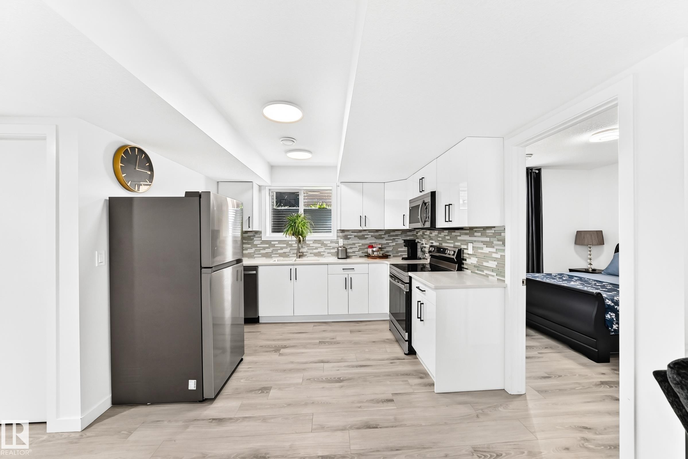 Modern kitchen featuring white cabinetry, light wood-finish flooring, a mosaic tile backsplash, stainless steel appliances, and recessed lighting - 3672 Claxton Place Sw, Edmonton, AB